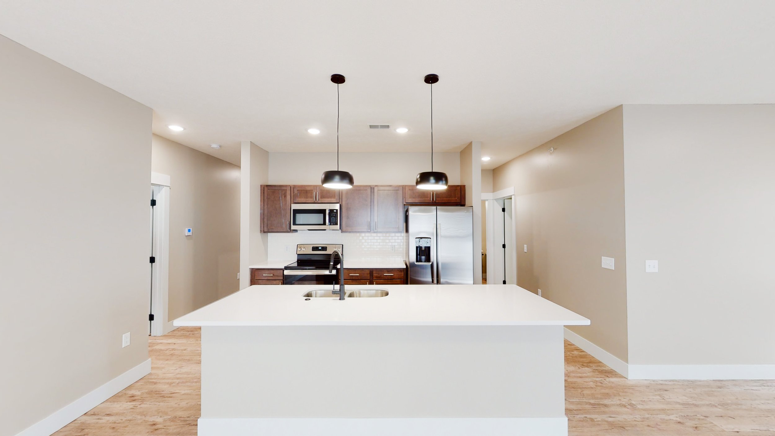 Modern kitchen with white island, stainless steel appliances, wooden cabinets, and pendant lights.