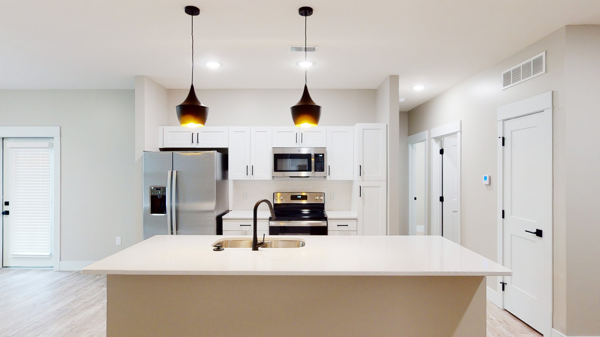 Modern kitchen with white cabinets, stainless steel appliances, and an island with a sink. Features pendant lights and a gray color scheme.