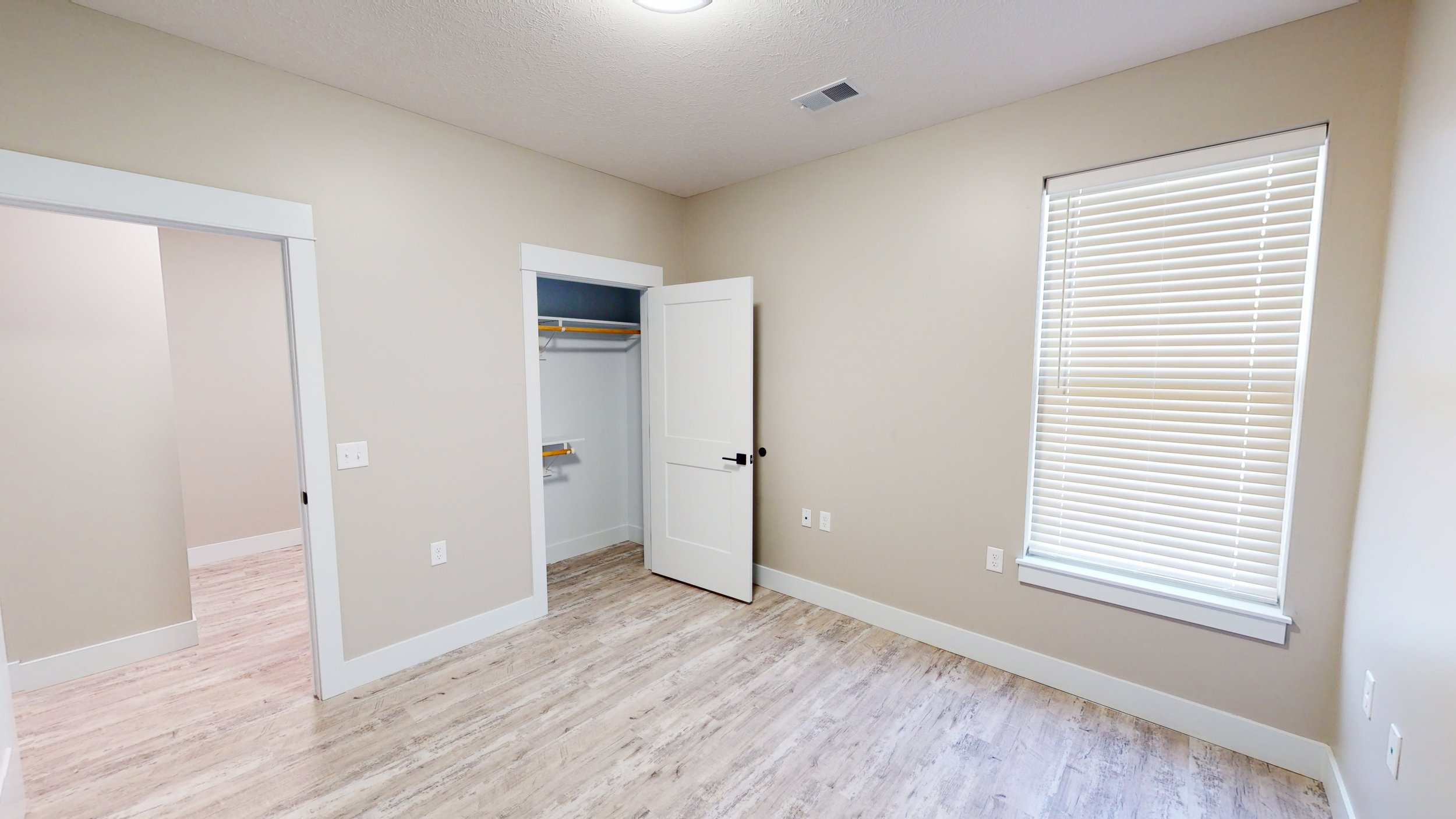 Empty room with beige walls, wood flooring, open closet with white door, and window with blinds.