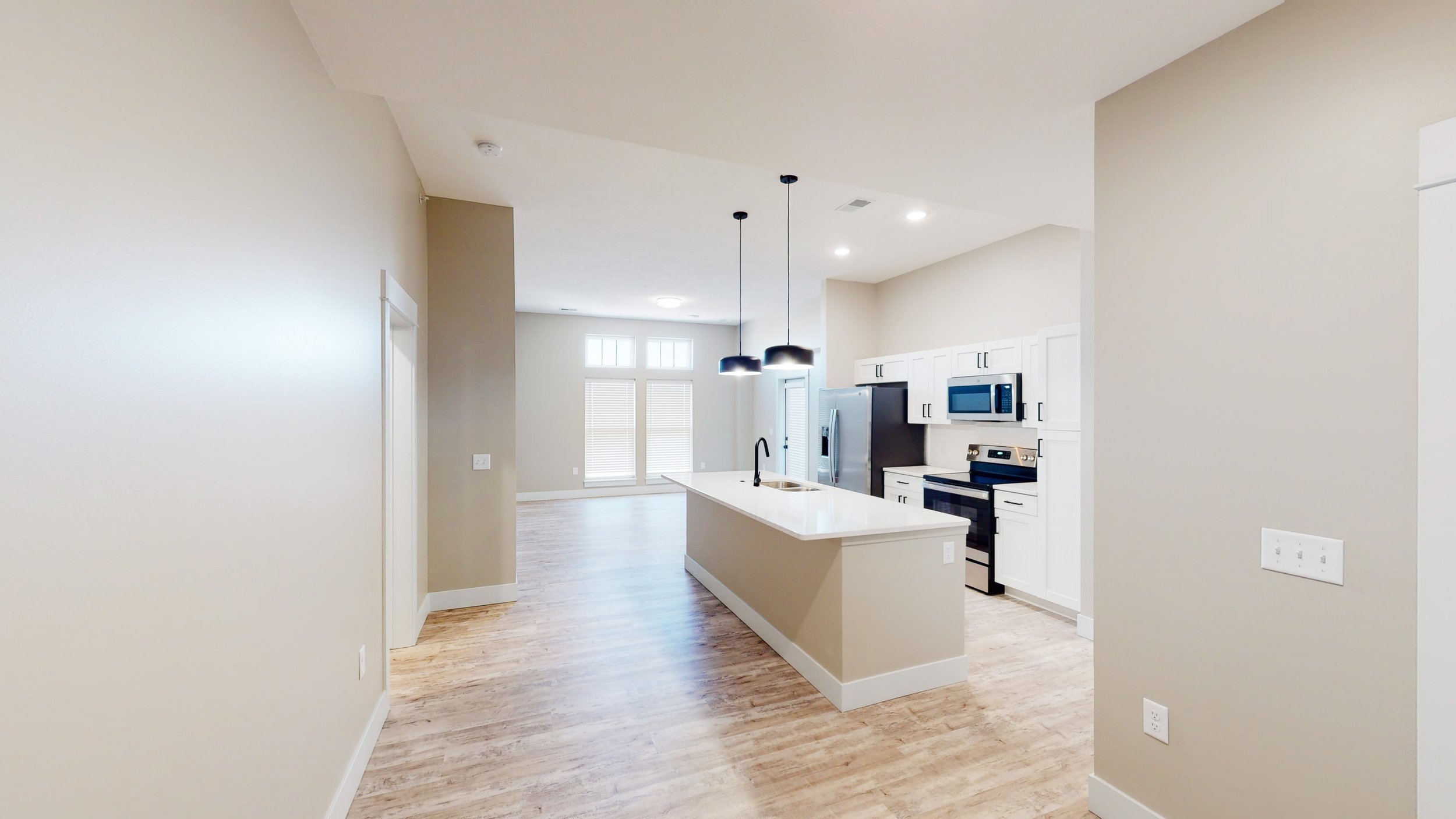 Modern kitchen and dining area with light wood flooring, tan walls, white cabinets, stainless steel appliances, and a central island with pendant lights.