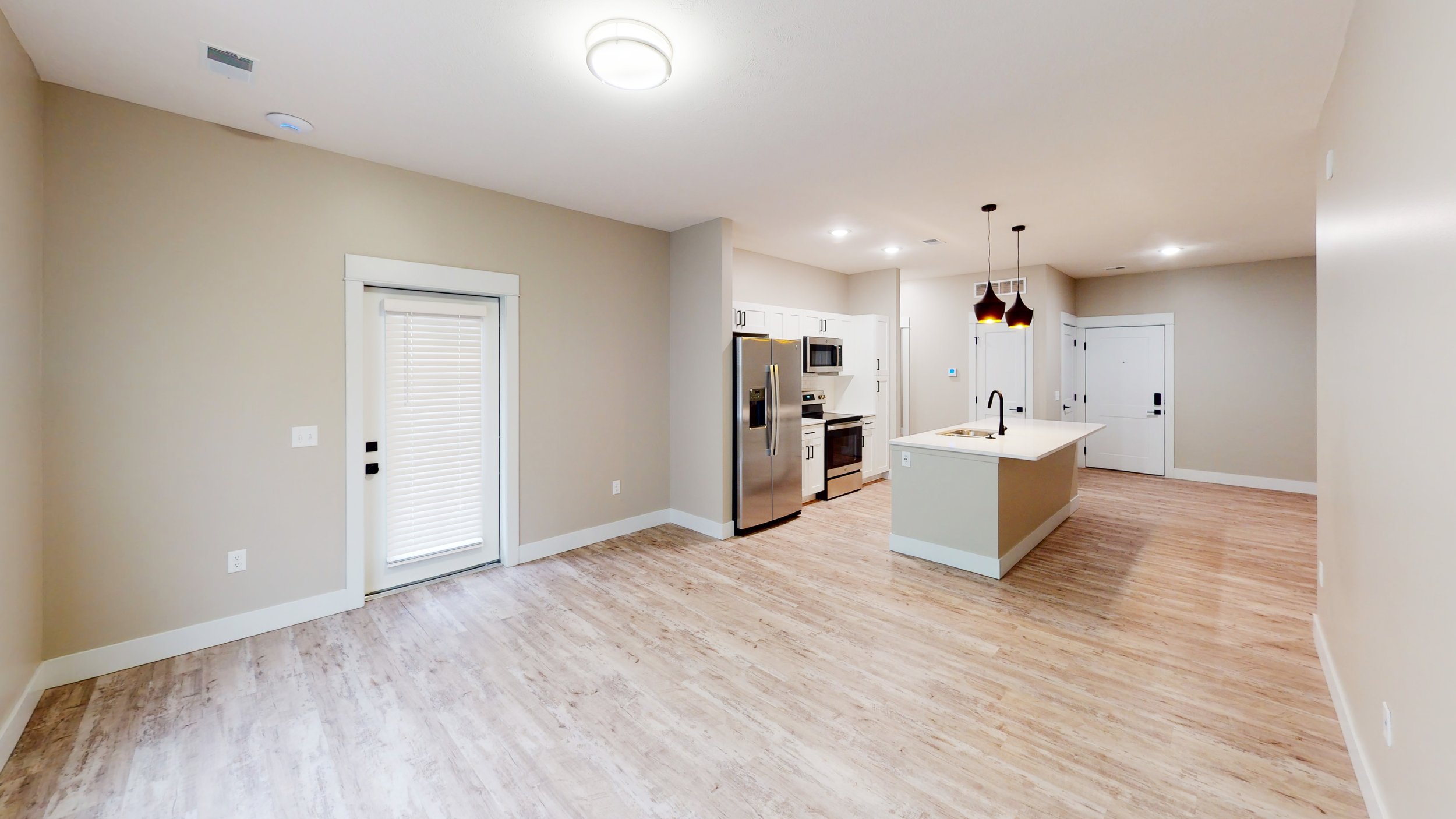Modern open-concept kitchen and living area with wood flooring, stainless steel appliances, island with pendant lights, and sliding glass door with blinds.