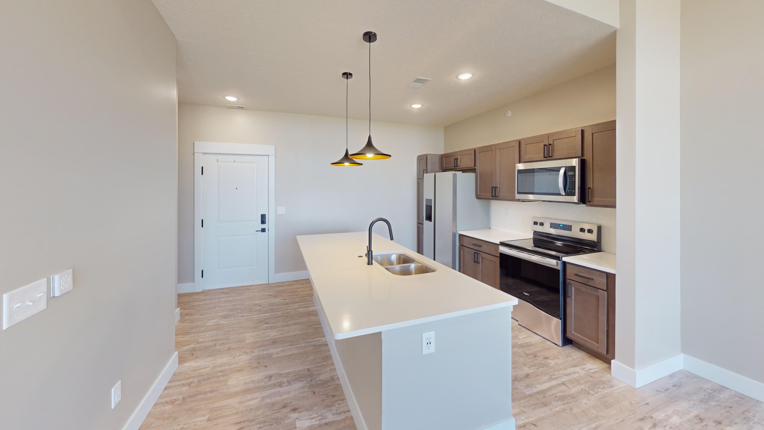 Modern kitchen with island, stainless steel appliances, wood cabinets, pendant lighting, and hardwood flooring.