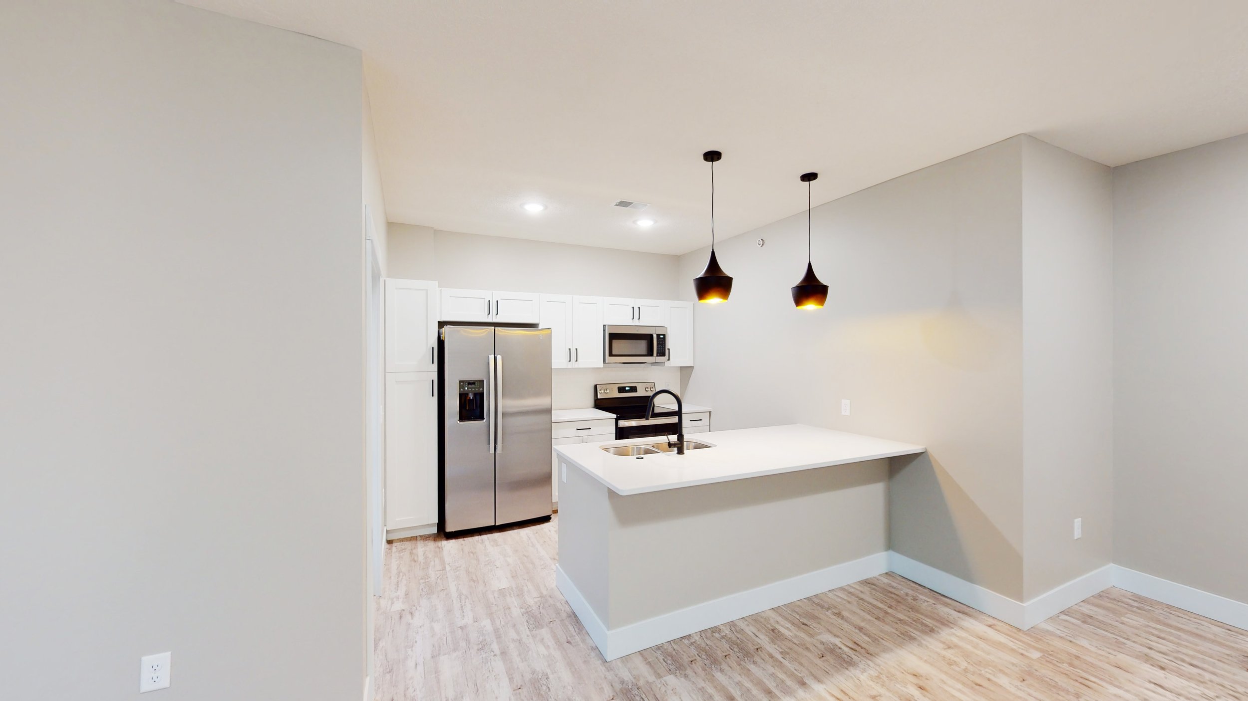 Modern kitchen with white cabinets, stainless steel appliances, pendant lights, and light wood flooring.