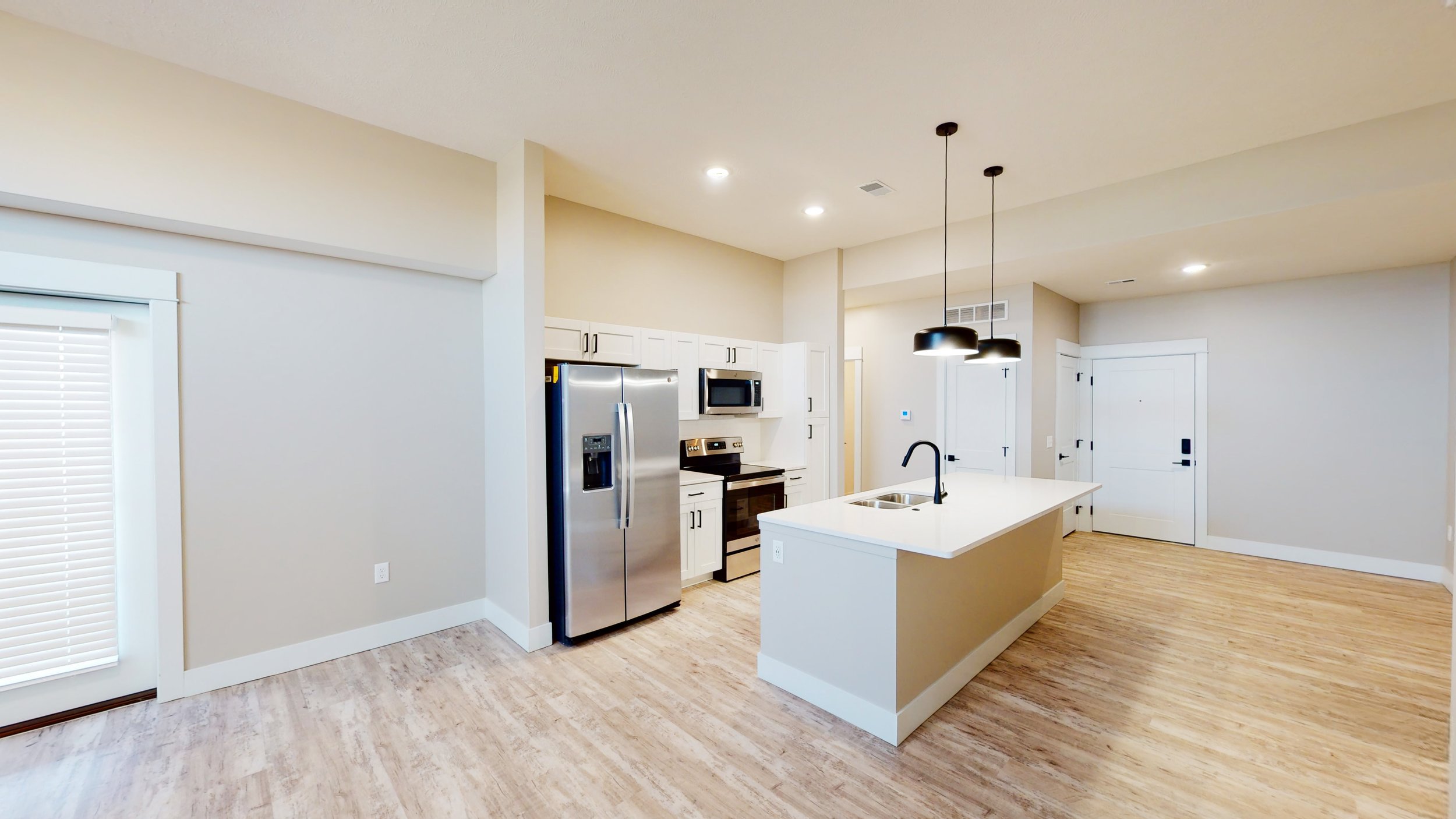 Modern kitchen interior with stainless steel appliances, white cabinets, and an island with pendant lights.