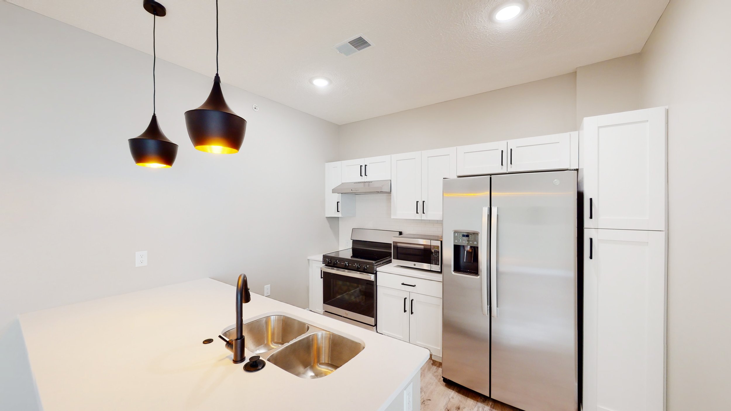 Modern kitchen with white cabinets, stainless steel appliances, double sink, and black pendant lights