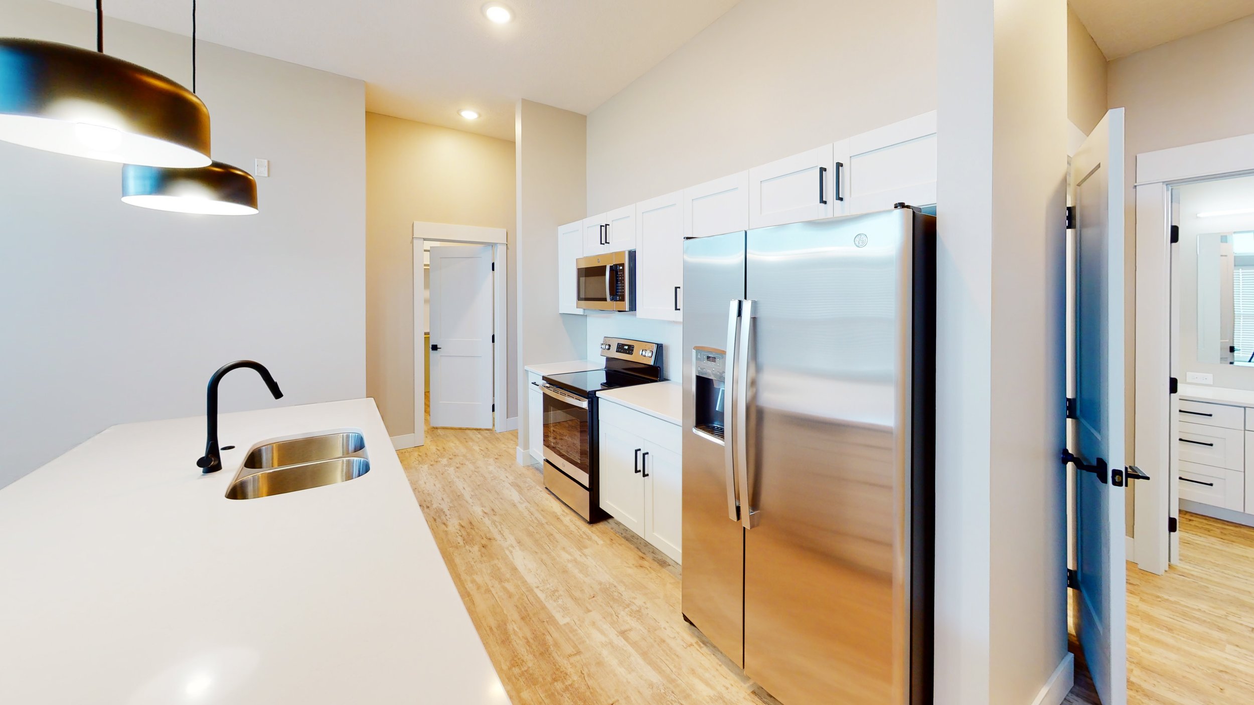 Modern kitchen with white cabinets, stainless steel appliances, and wooden floor.