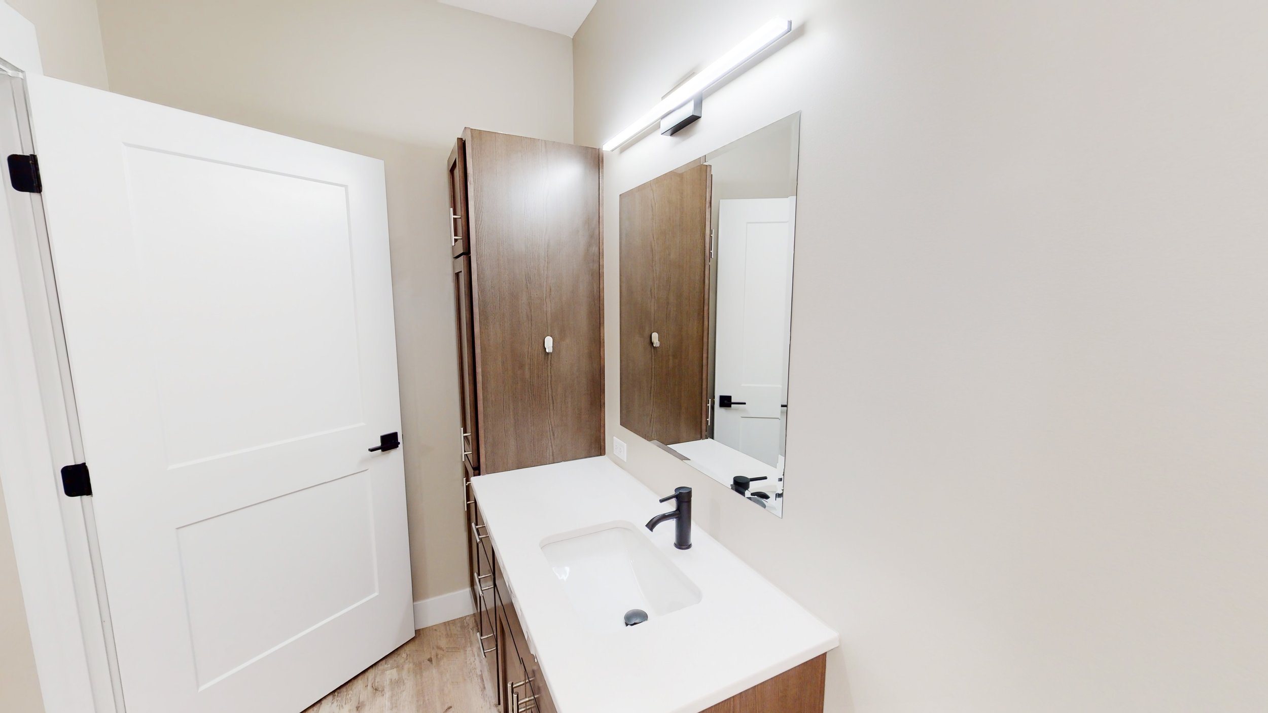 Modern bathroom with a white countertop, brown cabinets, a rectangular mirror, and a black faucet under bright lighting.