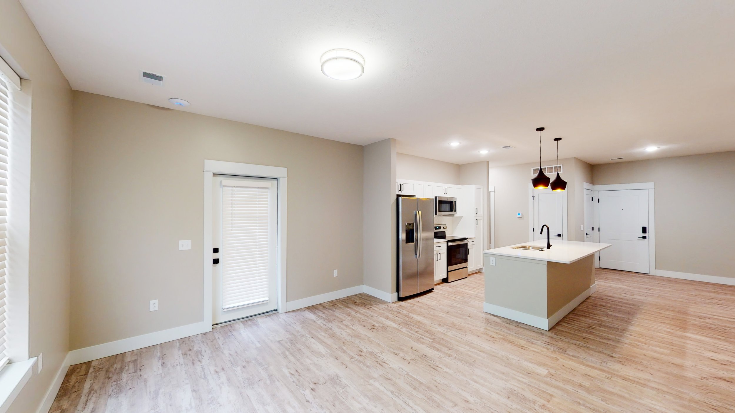 Modern kitchen and living area with hardwood floors, stainless steel appliances, and a kitchen island with pendant lights.