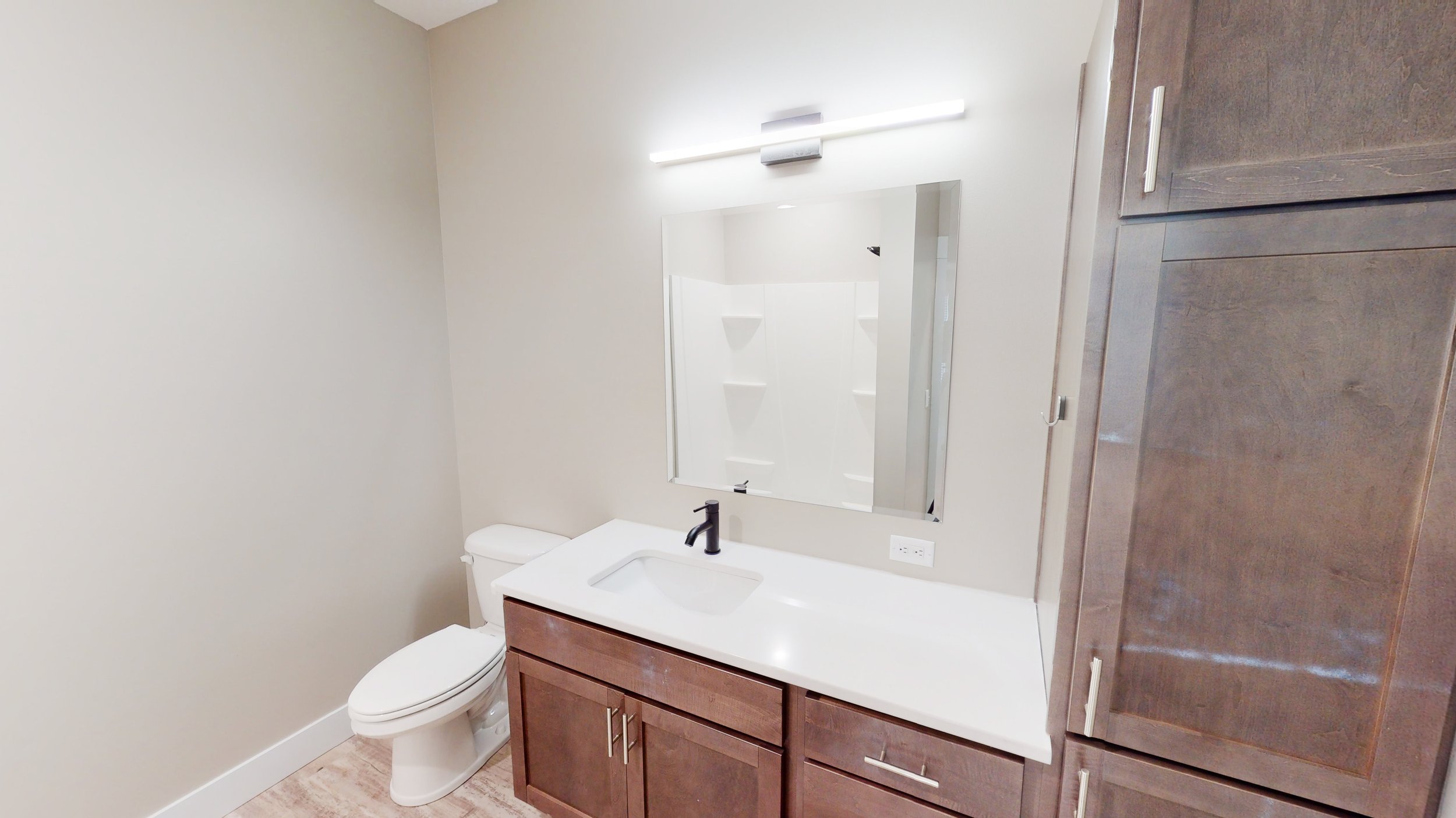 Modern bathroom with white sink, dark wood vanity, mirror, toilet, and shower.