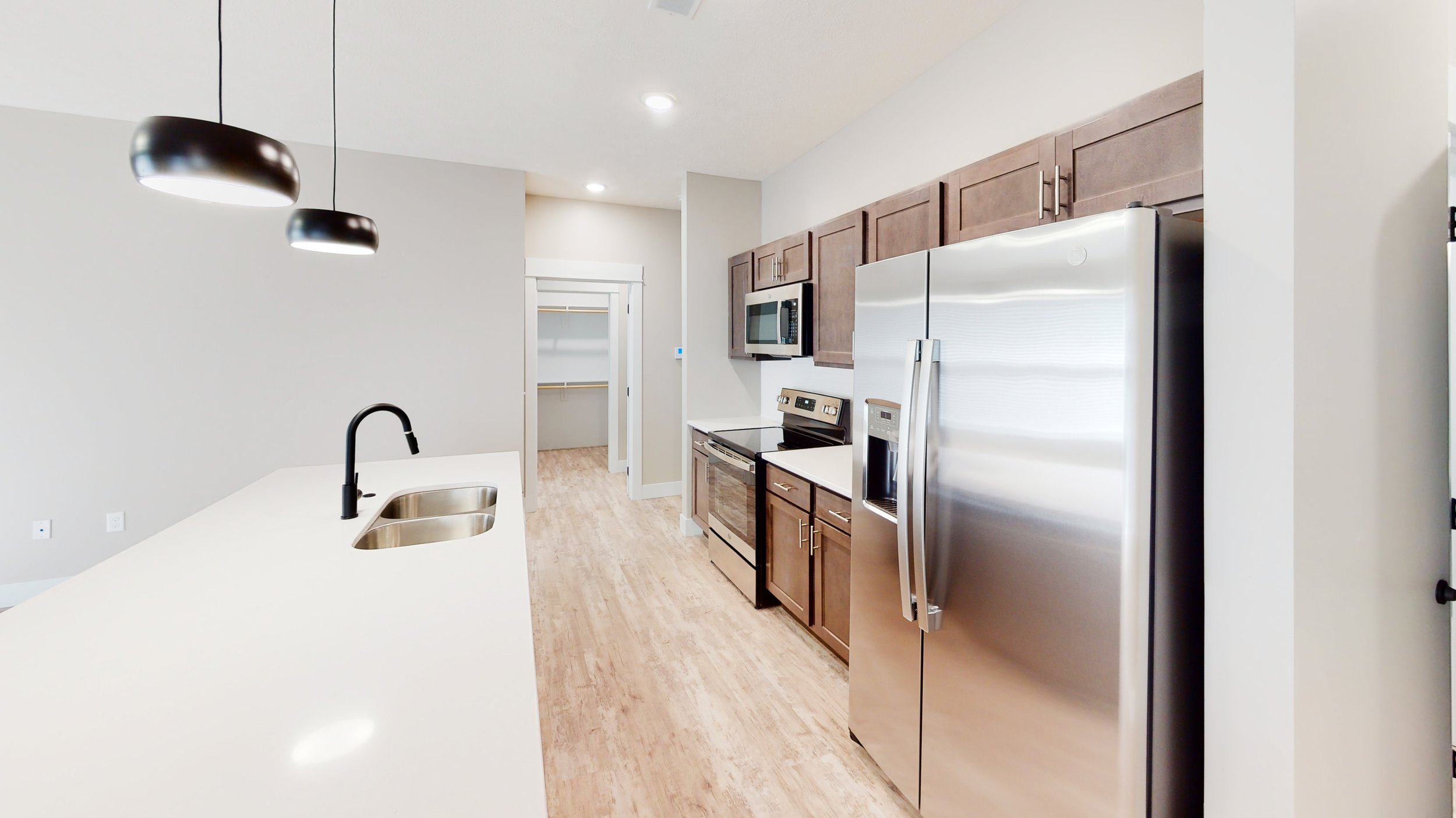 Modern kitchen with stainless steel appliances, including a refrigerator and oven, wood cabinets, a white countertop with a sink, and pendant lighting.