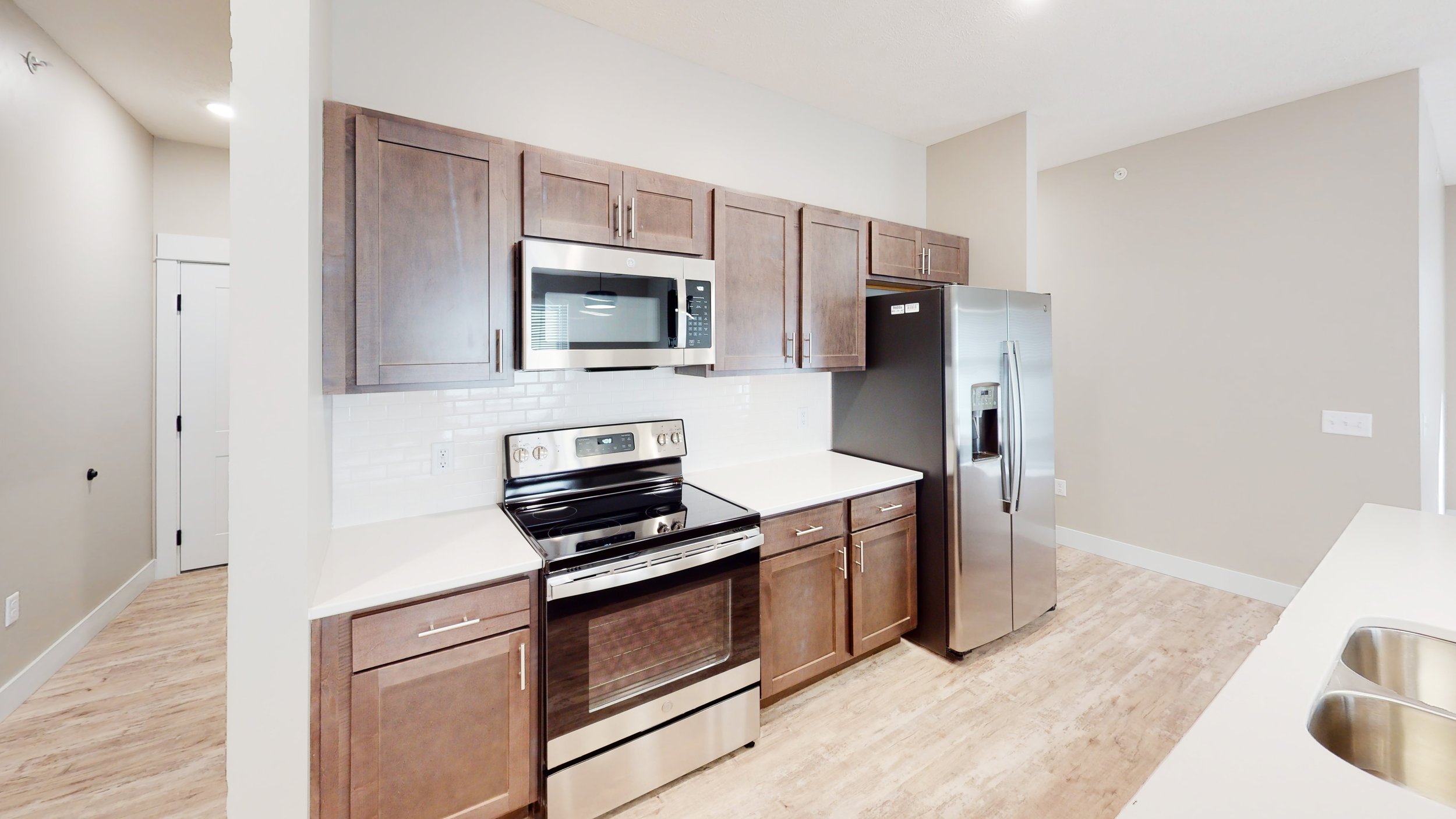 Modern kitchen with stainless steel stove, microwave, and refrigerator, brown cabinets, and white countertops.