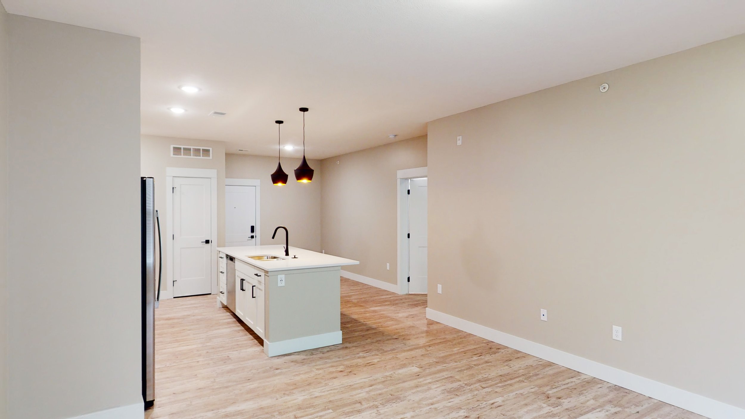Modern kitchen interior with island, pendant lighting, stainless steel refrigerator, and hardwood floors.