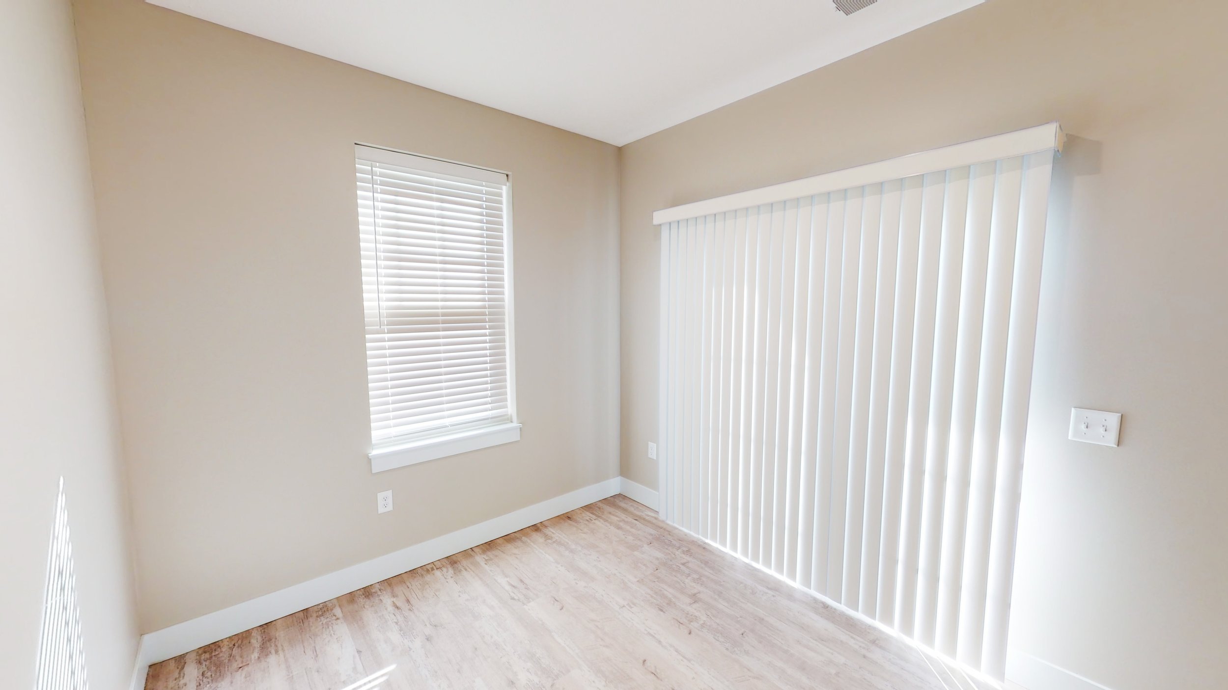Empty room with beige walls, hardwood floor, a window with blinds, and a sliding glass door with vertical blinds.