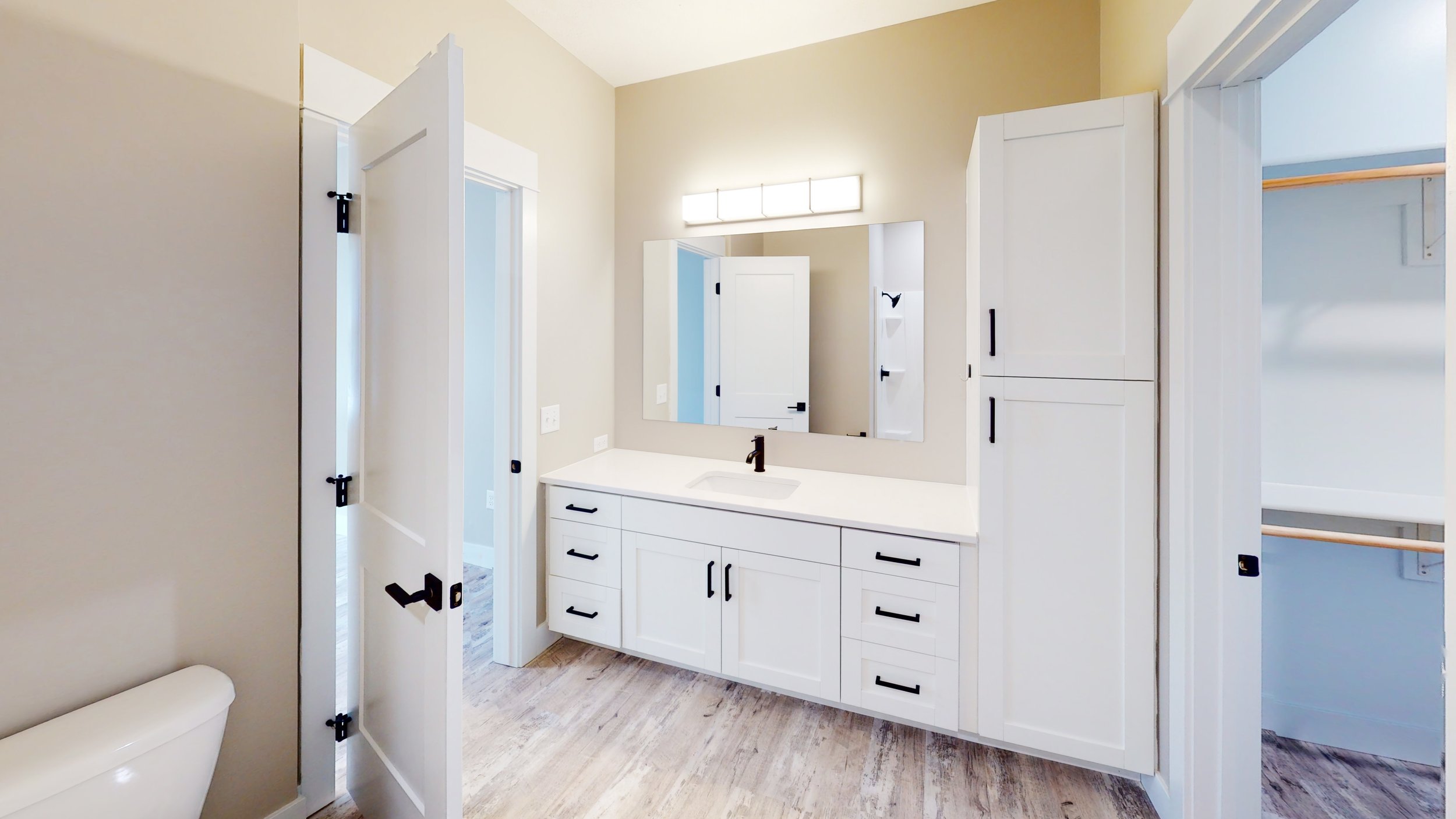 Modern bathroom with white cabinetry, large mirror, and open door.