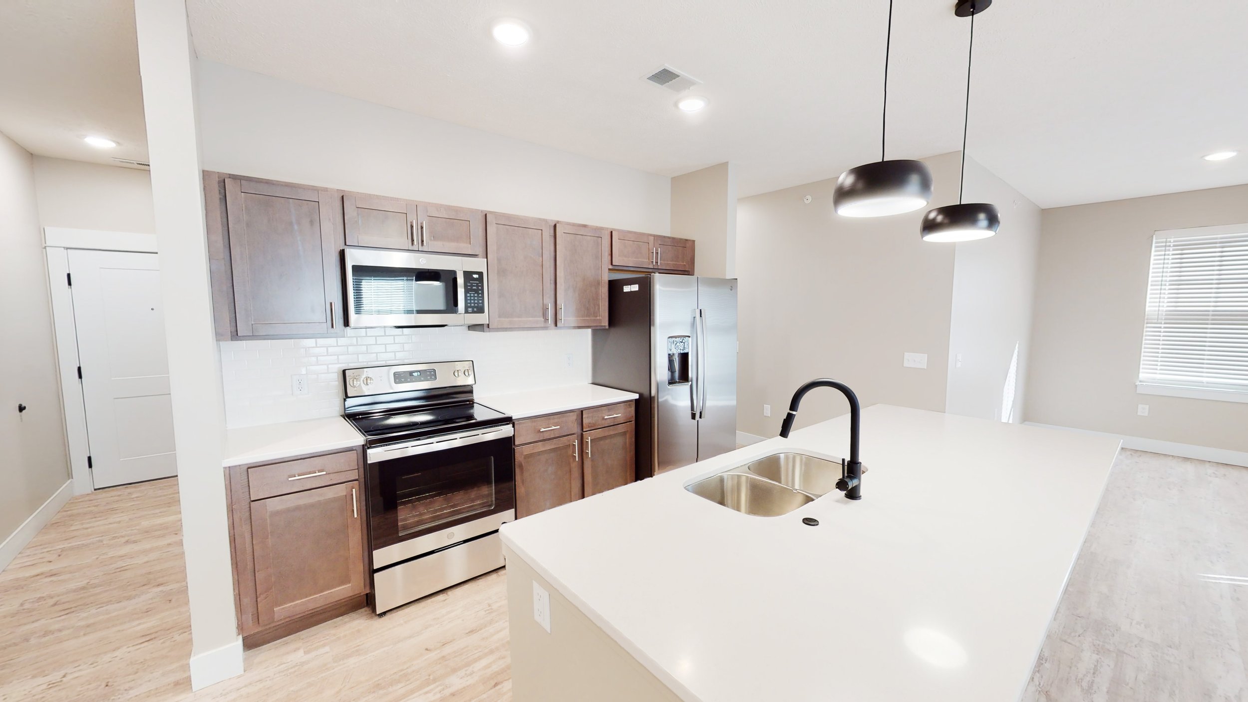 Modern kitchen with stainless steel appliances, wooden cabinets, white countertops, double sink, and pendant lighting.