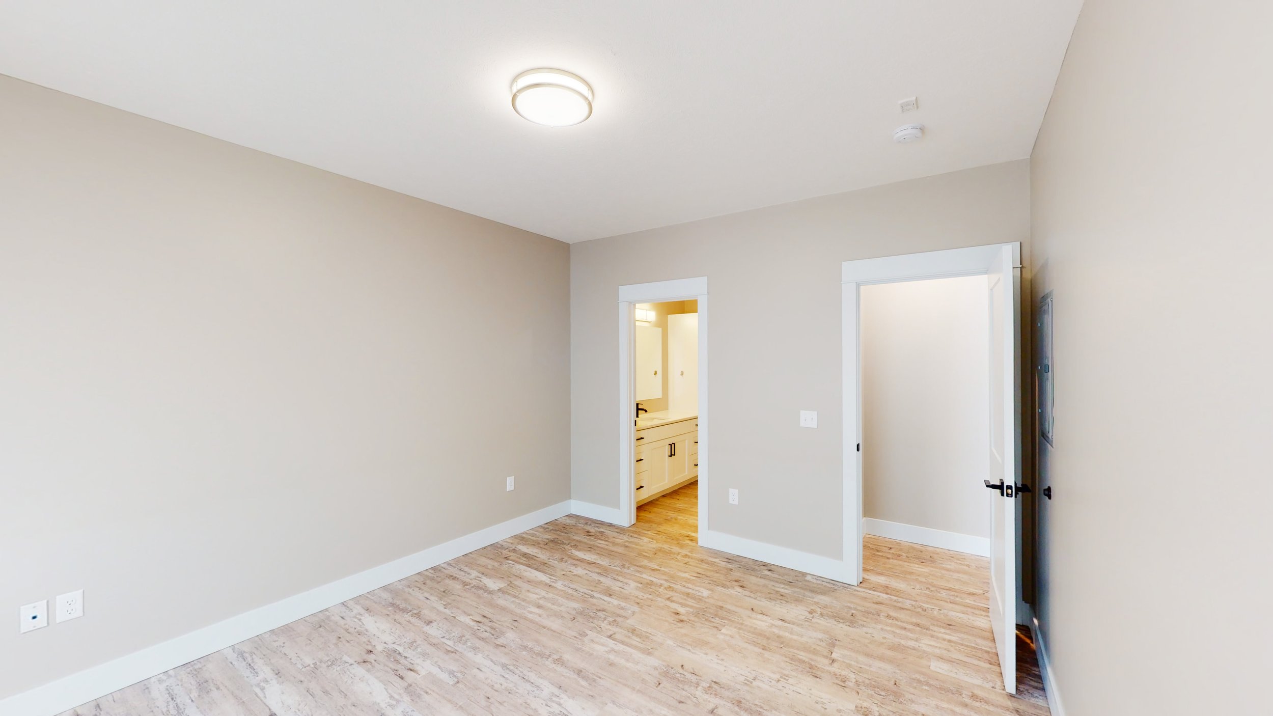 Empty room with wooden floor, beige walls, and two doorways leading to a bathroom and a closet.