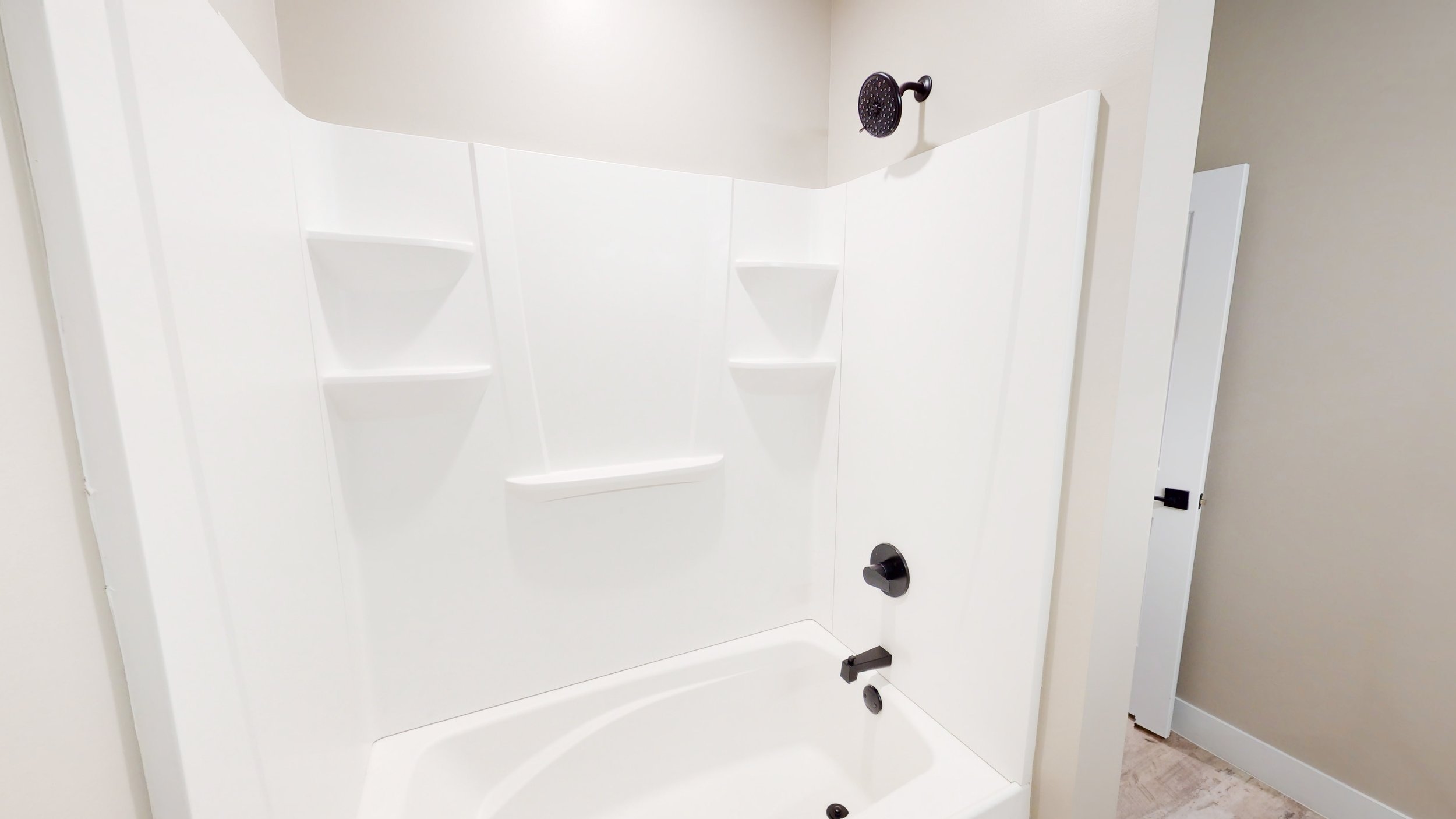Modern white bathtub and shower with corner shelves and black fixtures.