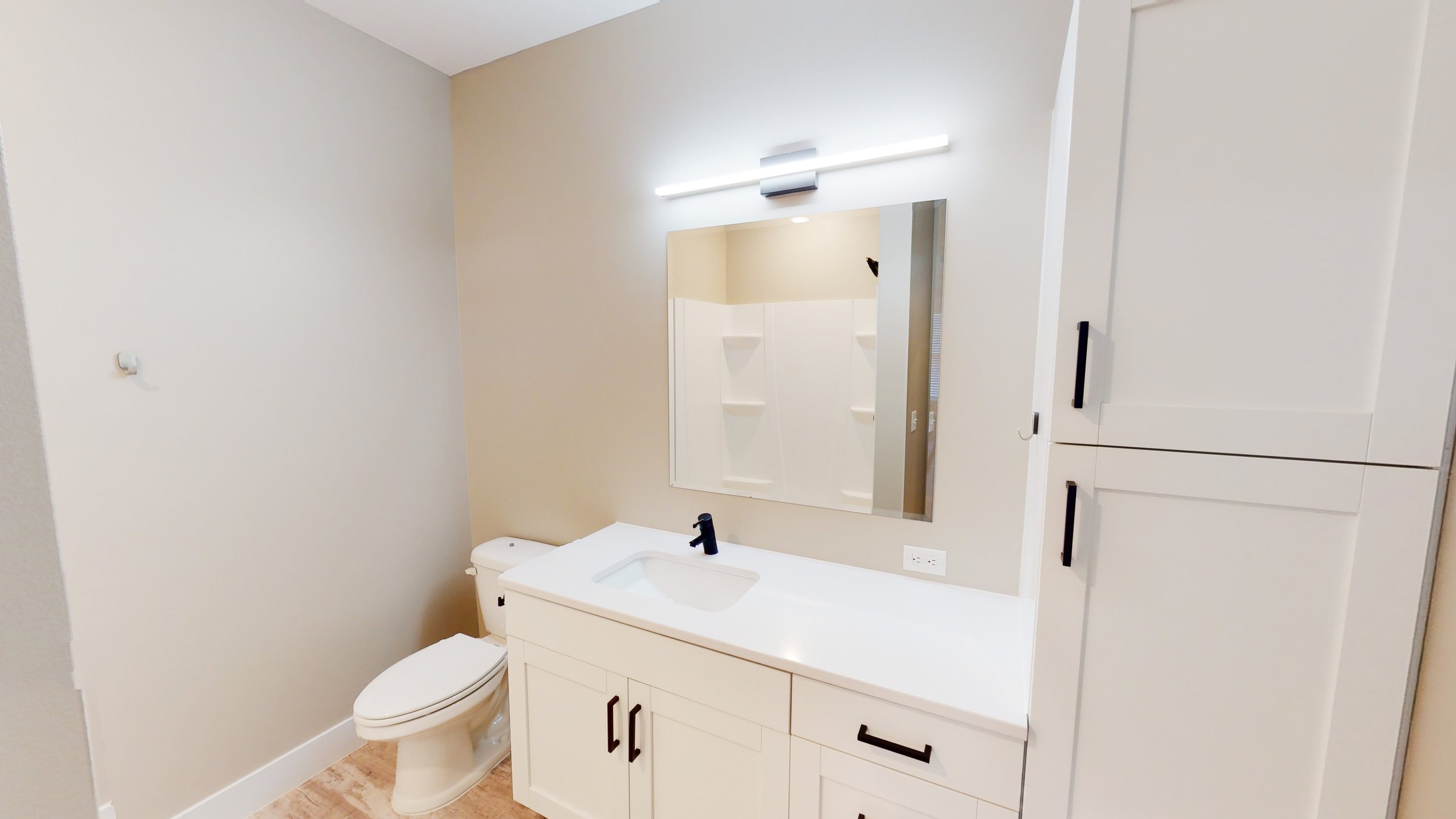 Modern bathroom with white vanity, mirror with overhead light, toilet, and storage cabinets.