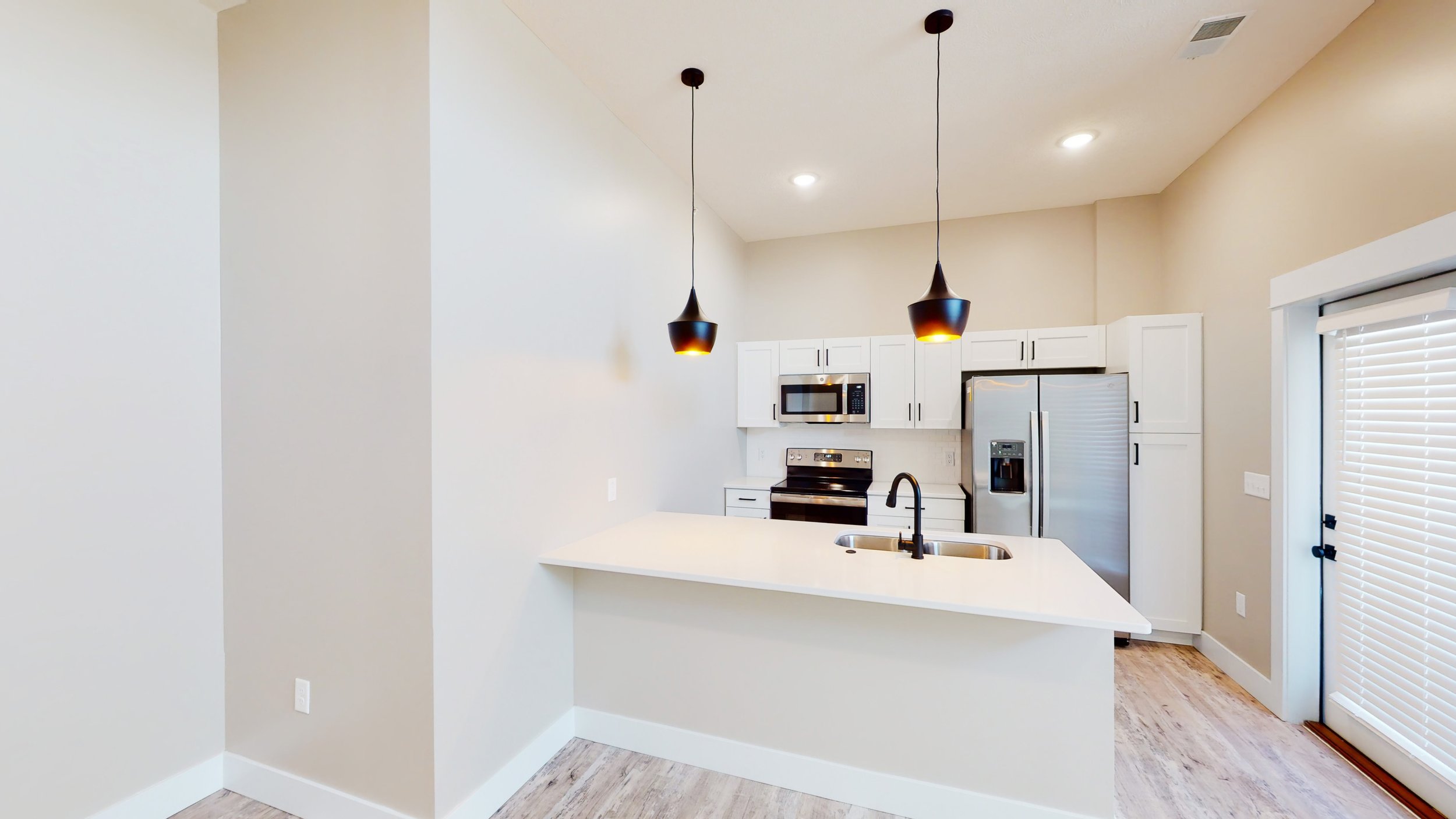 Modern kitchen with white cabinets, stainless steel appliances, and pendant lights over an island with sink.