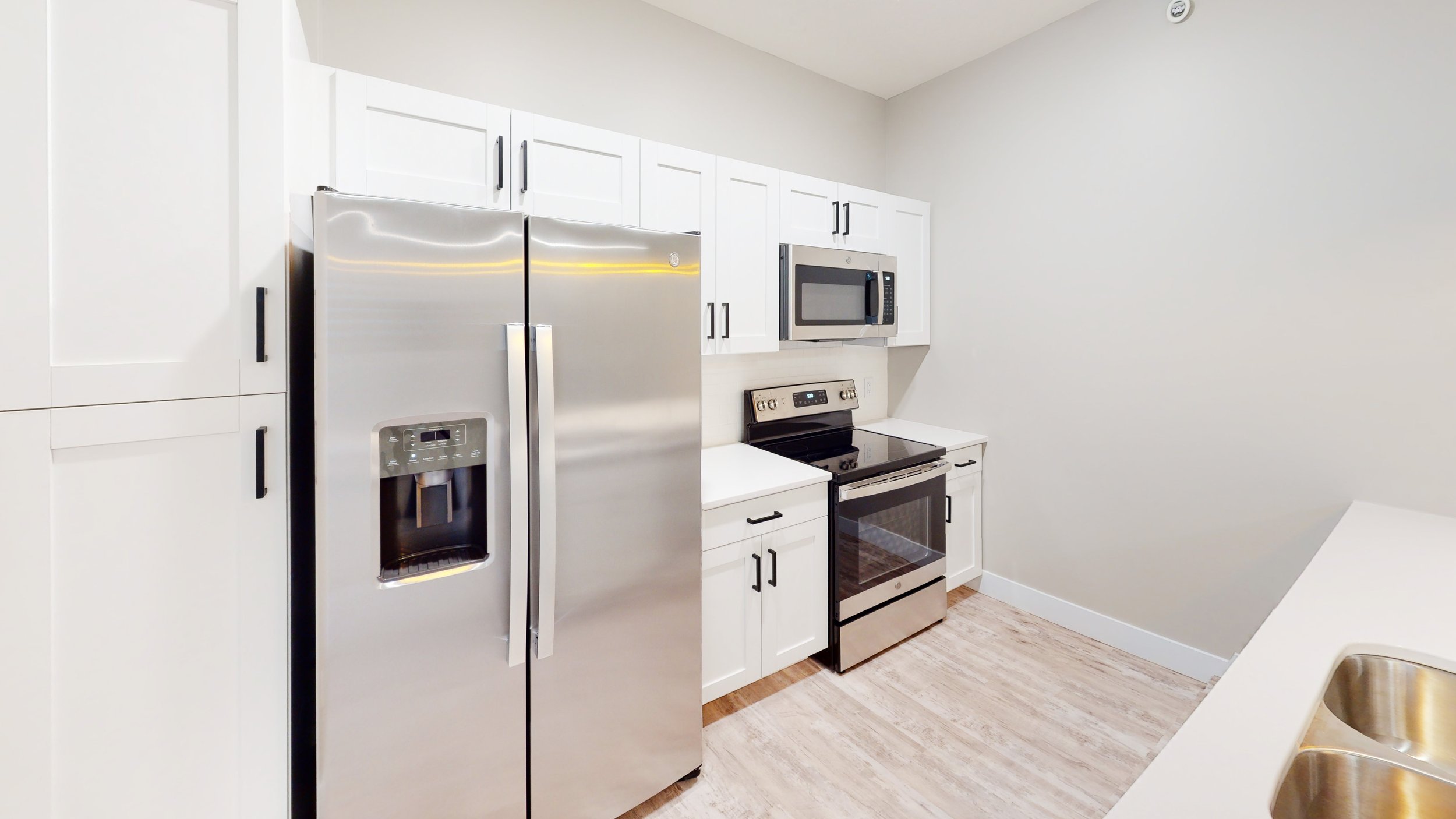 Modern kitchen with stainless steel refrigerator, electric stove, microwave, and white cabinetry.