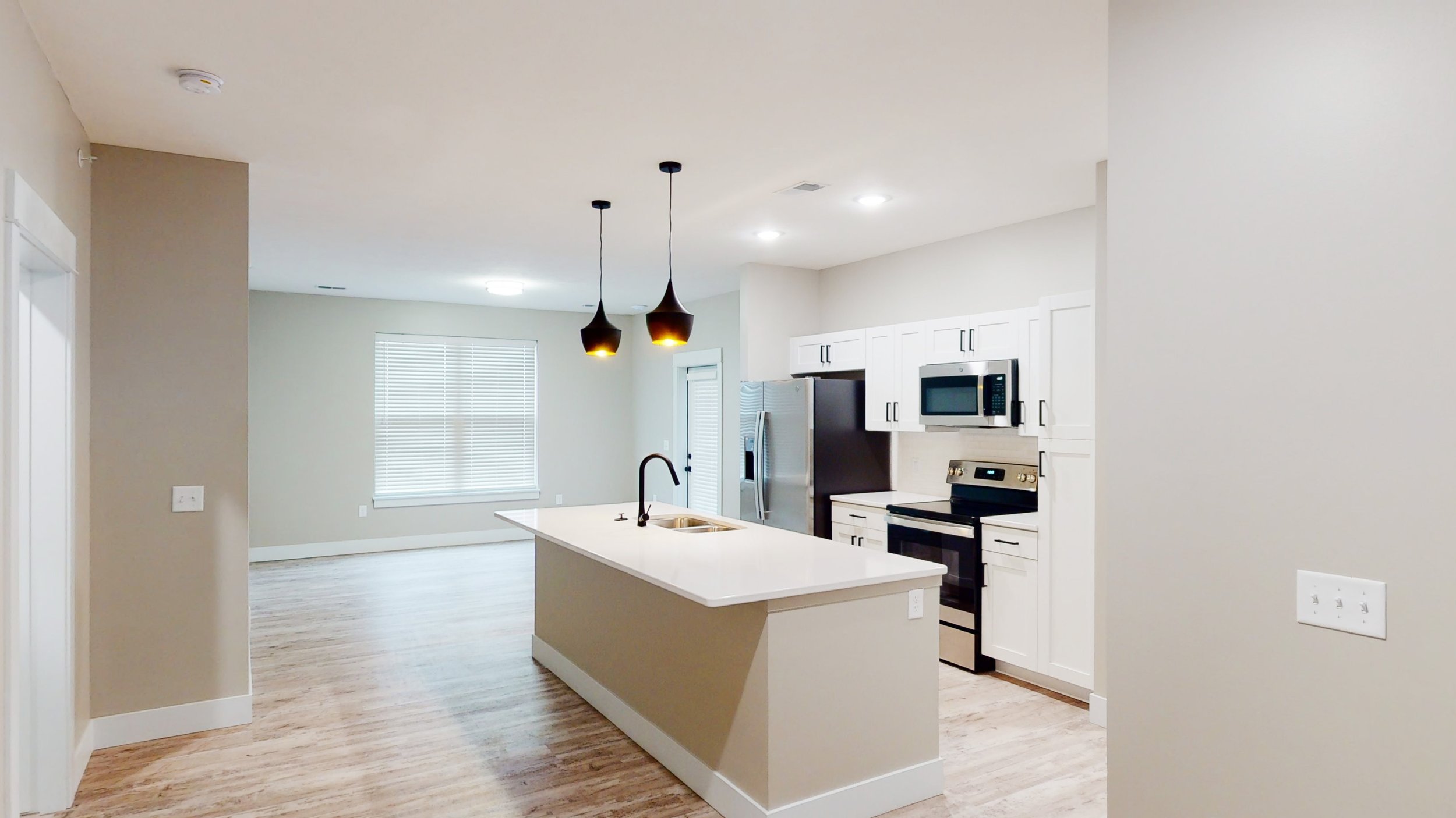 Modern kitchen with island, pendant lights, stainless steel appliances, white cabinets, and hardwood floors.