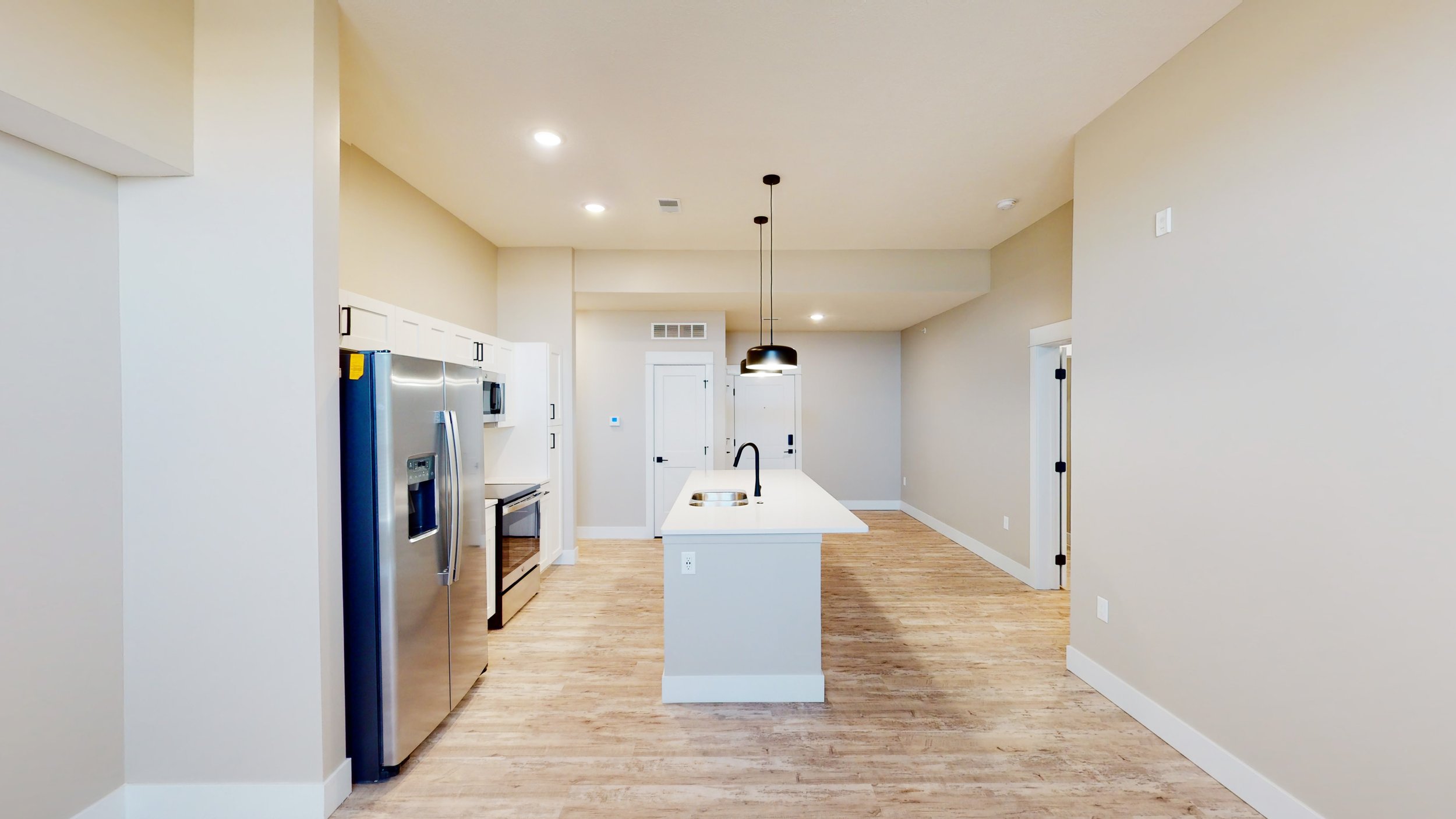 Modern kitchen with stainless steel appliances, white island, pendant lights, and wooden flooring.