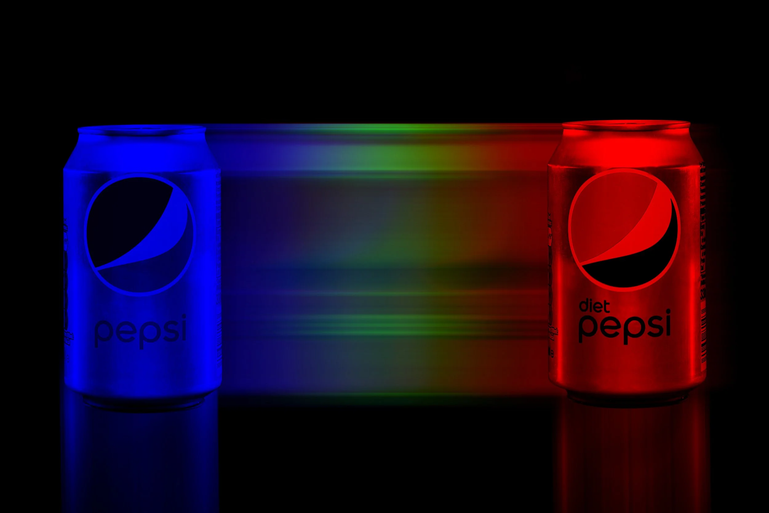 Two cans of Diet Pepsi, one blue and one red, are shown in a dark setting with light emitting from the cans, creating reflections on a surface. A colorful light streak, transitioning from blue to green to red, is visible between the cans.