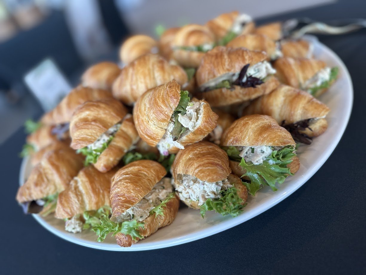 Plate of mini croissant sandwiches with lettuce and cream cheese on a black table.