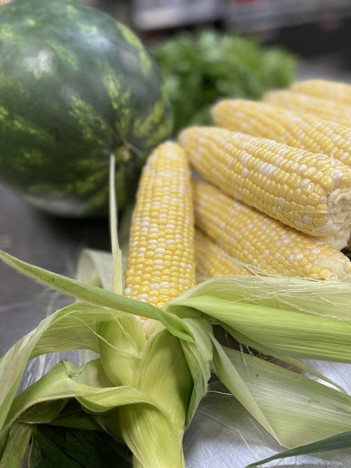 Fresh corn on the cob, a watermelon, and a head of lettuce on a metal surface.