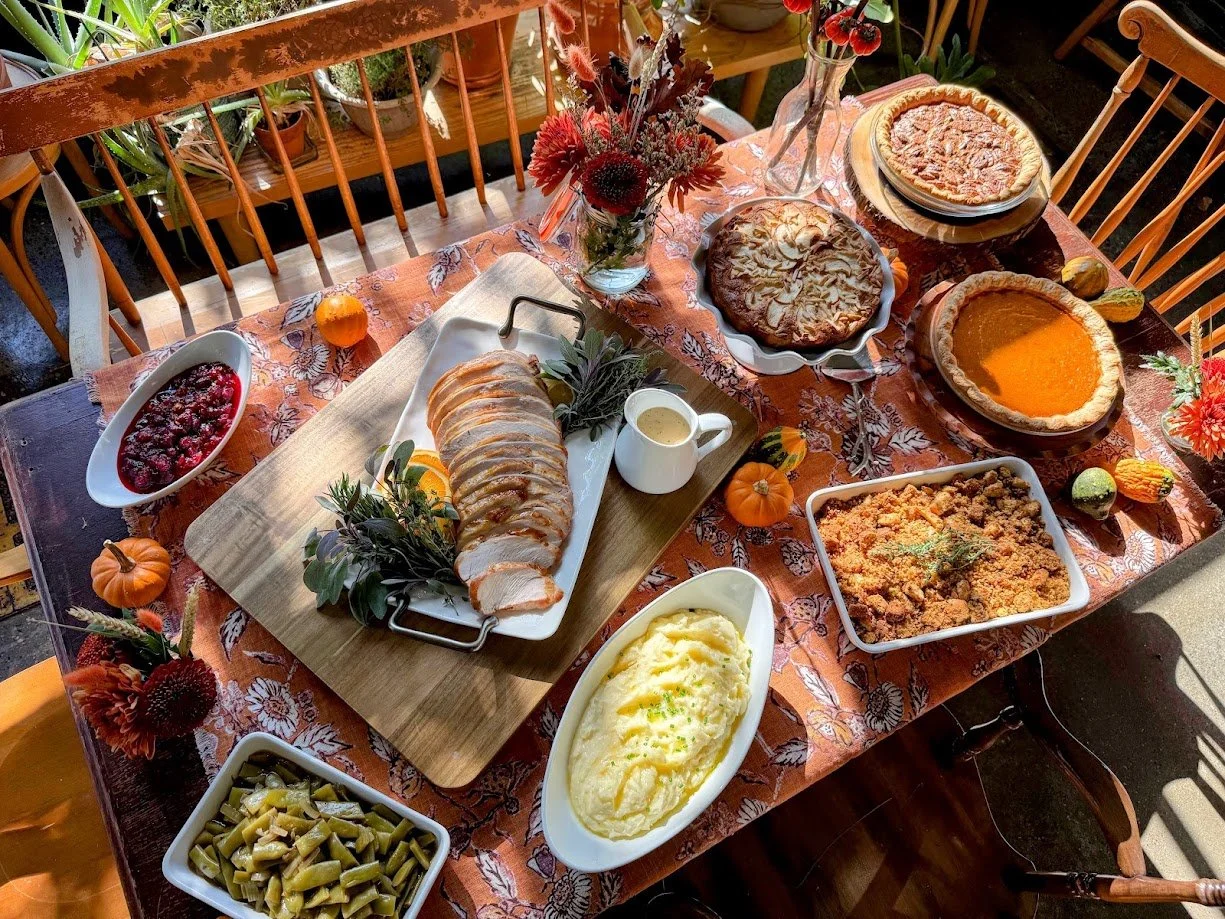 Thanksgiving dinner table with sliced turkey, cranberry sauce, pumpkin pie, casseroles, mashed potatoes, green beans, and autumn flowers
