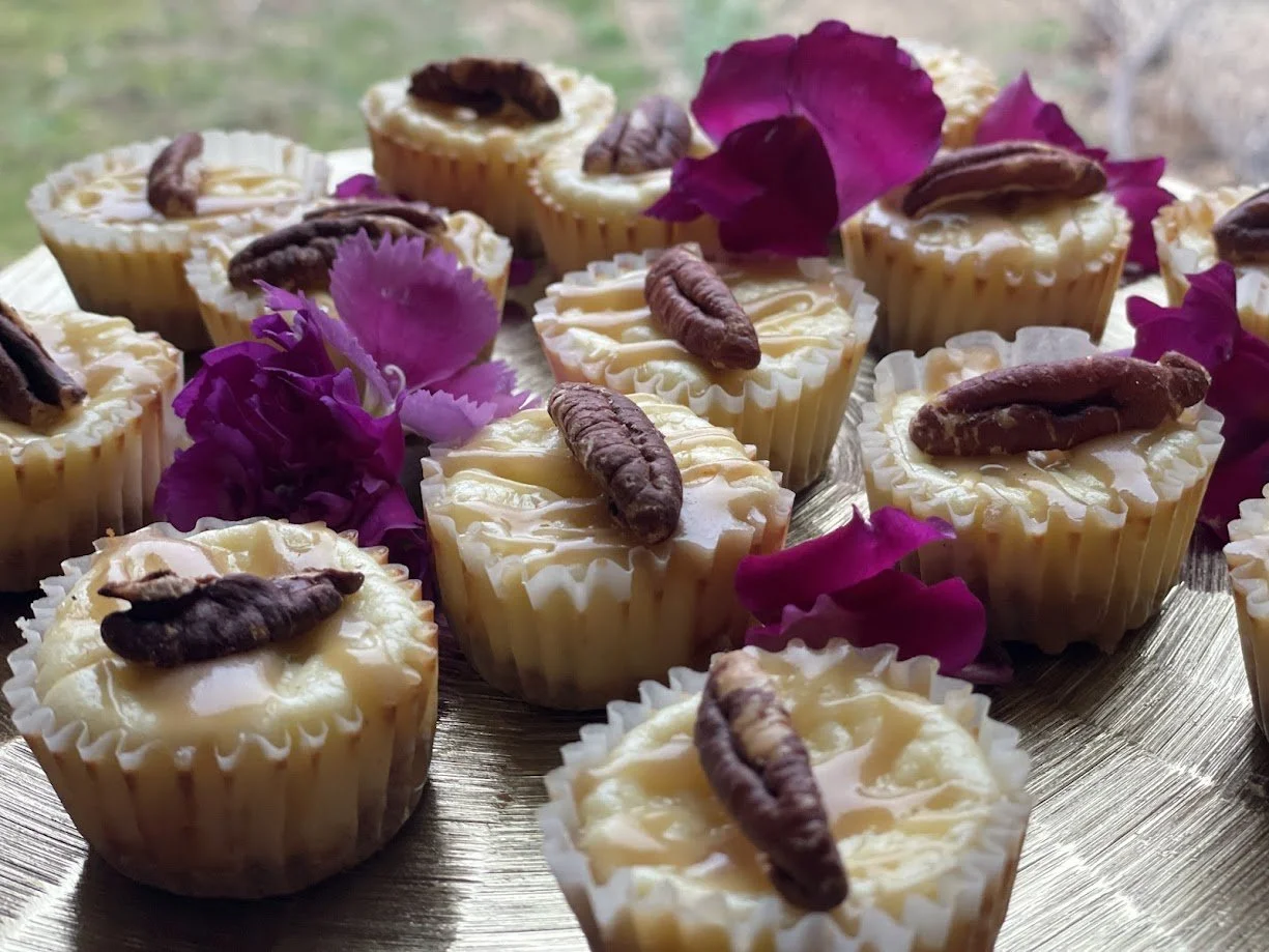 Cream cheese and pecan cup desserts decorated with purple flower petals on a silver tray.