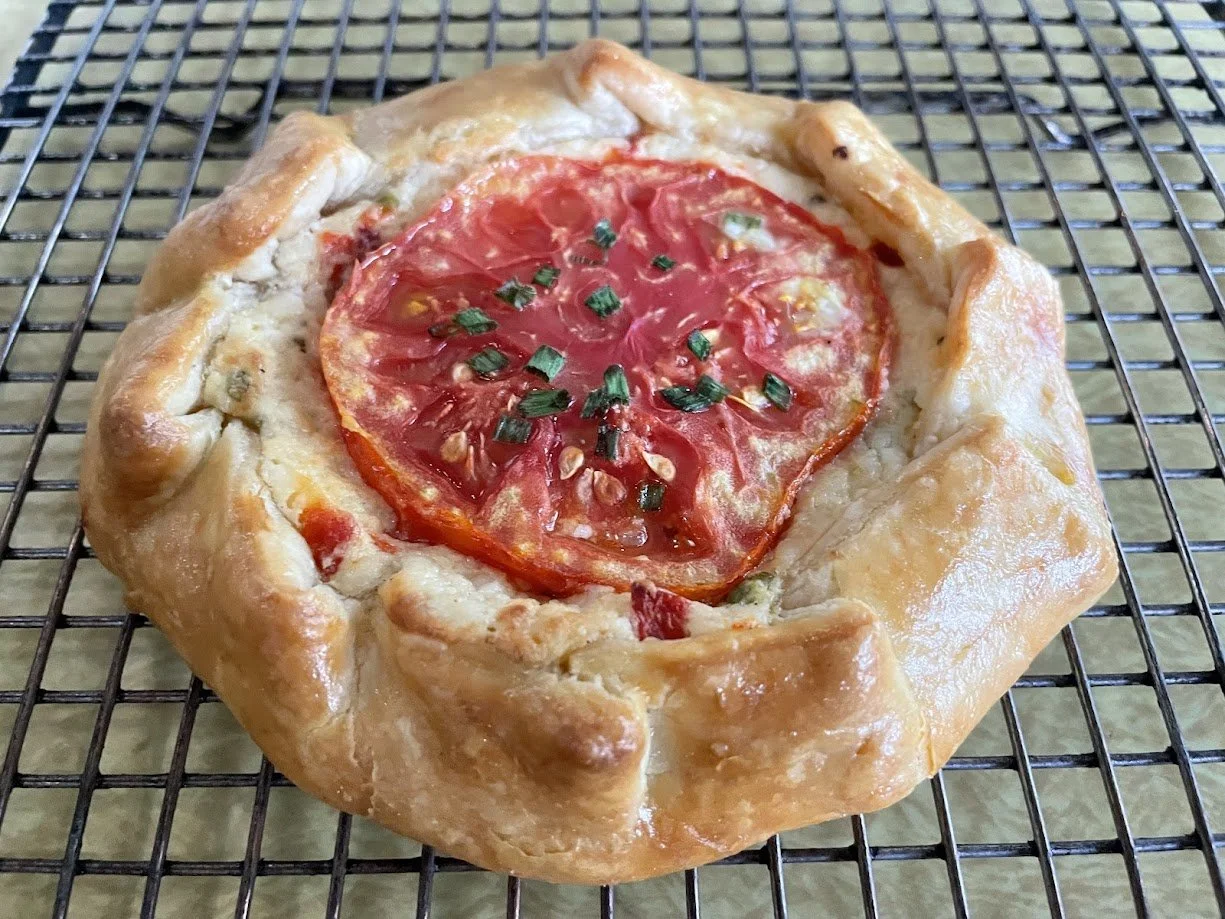 A rustic tomato galette with a golden, flaky crust on a wire cooling rack.