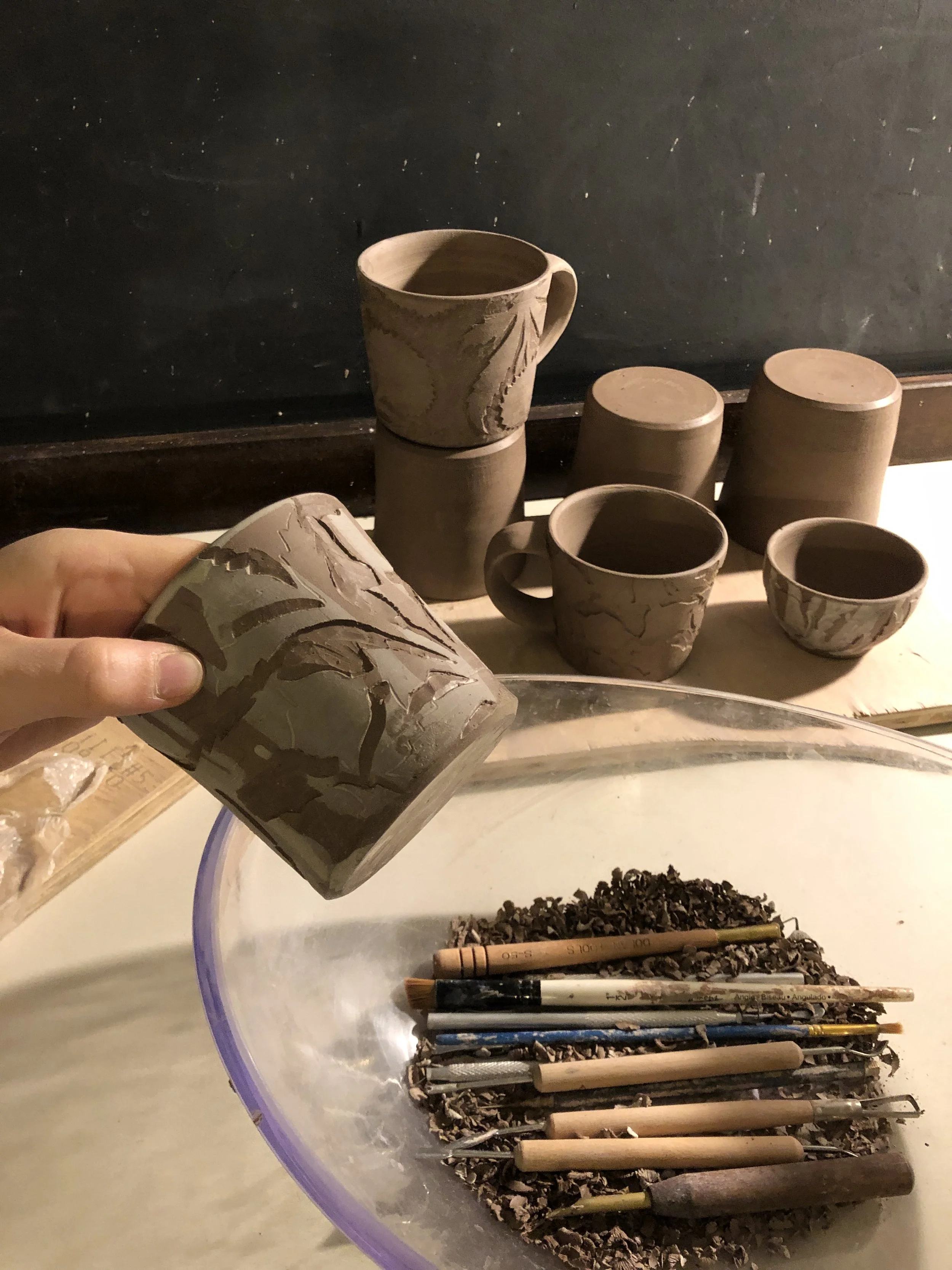 Hand carved pottery in progress with carving tools on a studio table 