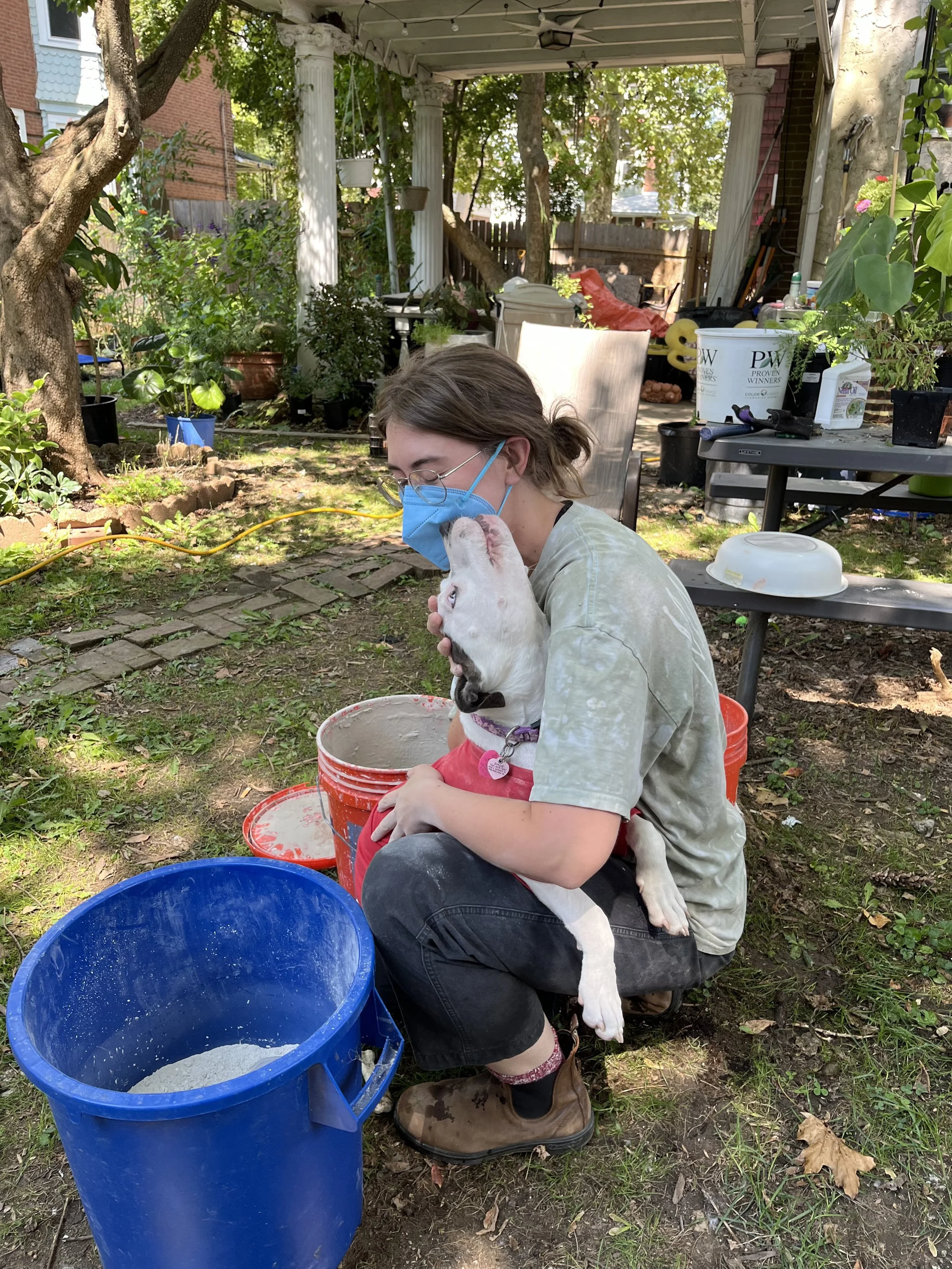 Artist, Vivian Purcell mixing glaze outdoors with help from dog