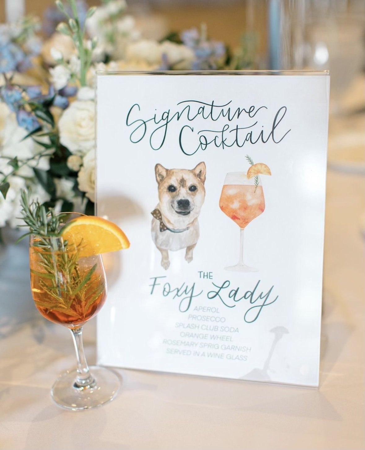 Signboard with a dog illustration and a cocktail menu featuring a signature drink called 'The Foxy Lady' alongside a cocktail glass with an orange slice garnish.
