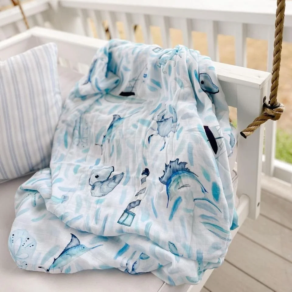 A rocking chair with a blanket featuring ocean animals like dolphins and whales draped over the side, on a porch with a white railing.