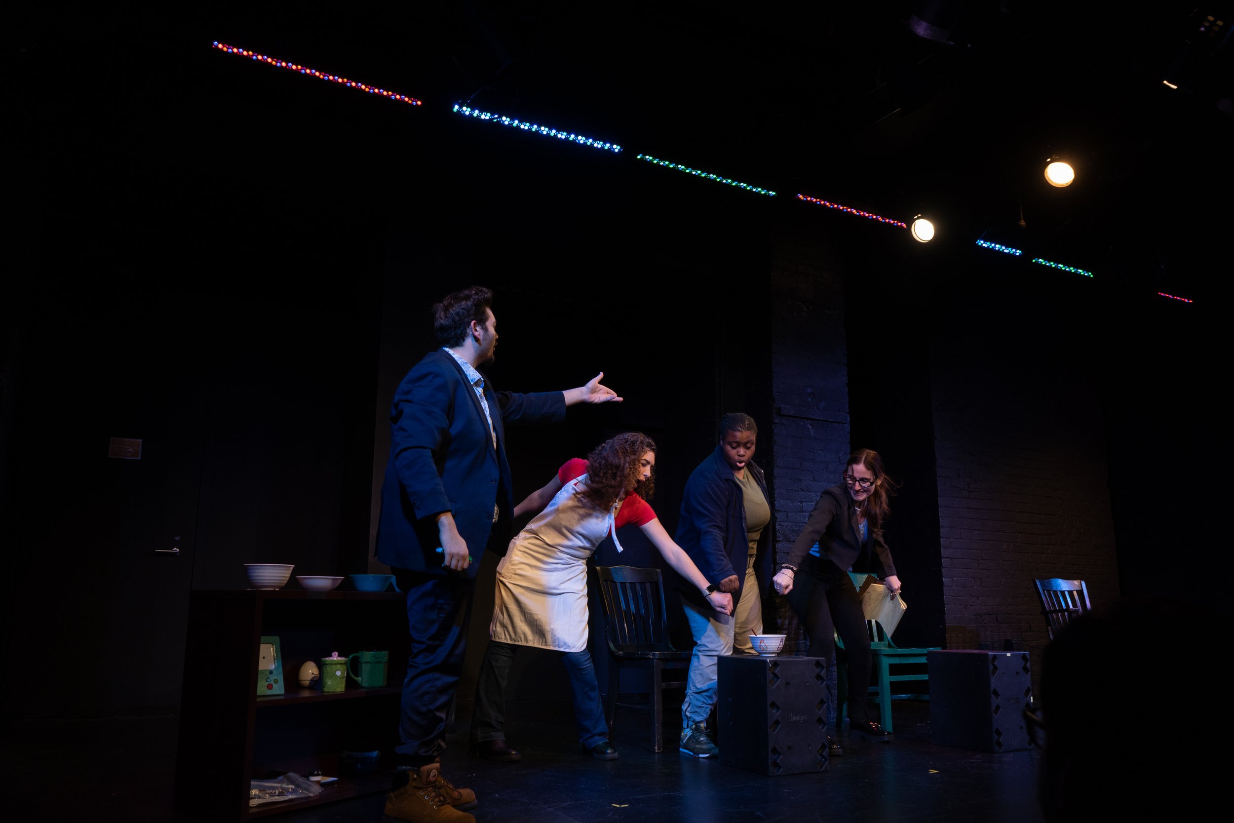 still from staged piece, featuring four actors with their hands gathering together