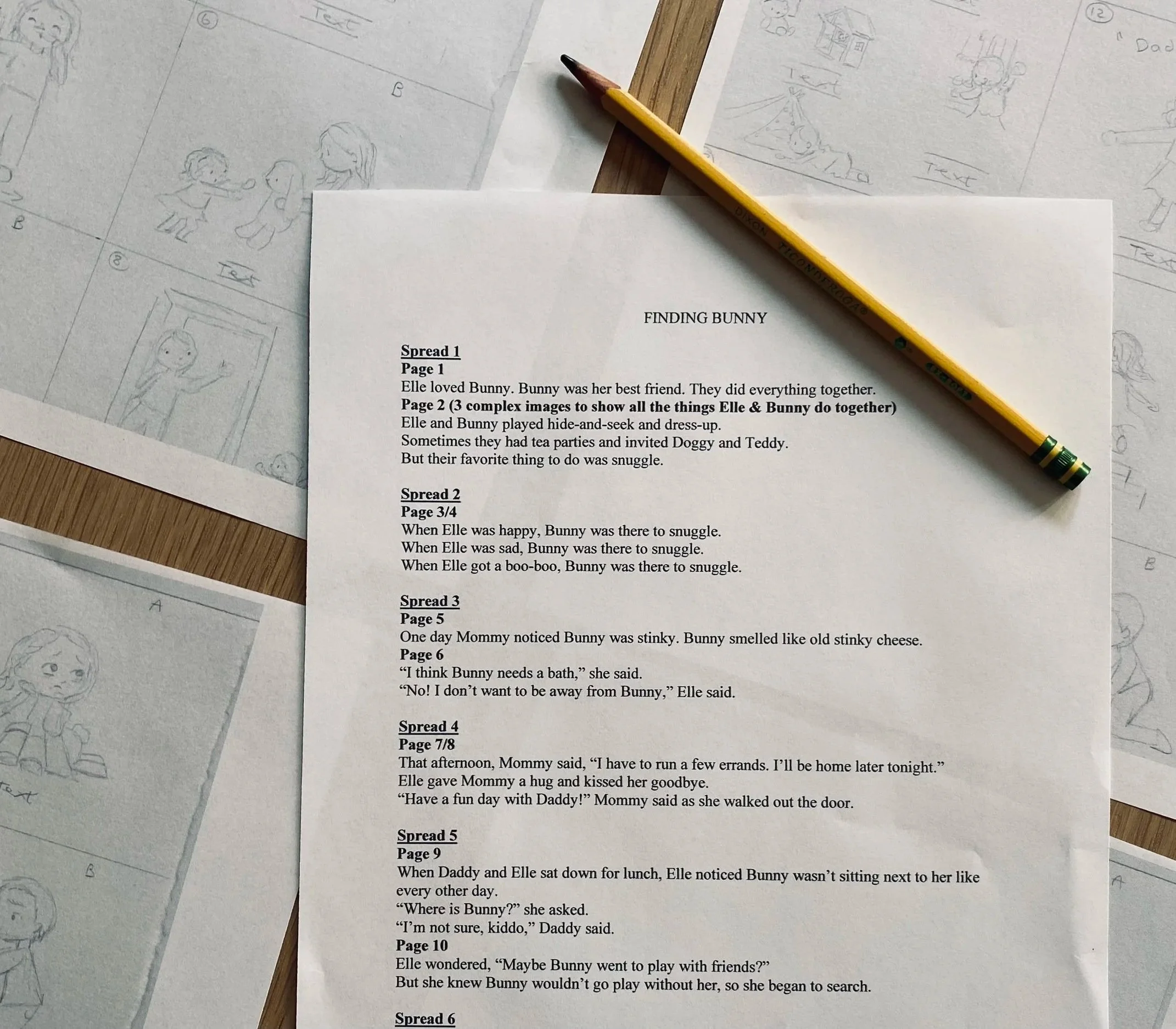 A printed story titled 'Finding Bunny' with multiple page spreads listing a story about Elle and her bunny, with handwritten sketches of children and animals on papers surrounding a wooden table, a yellow pencil resting on the story page.