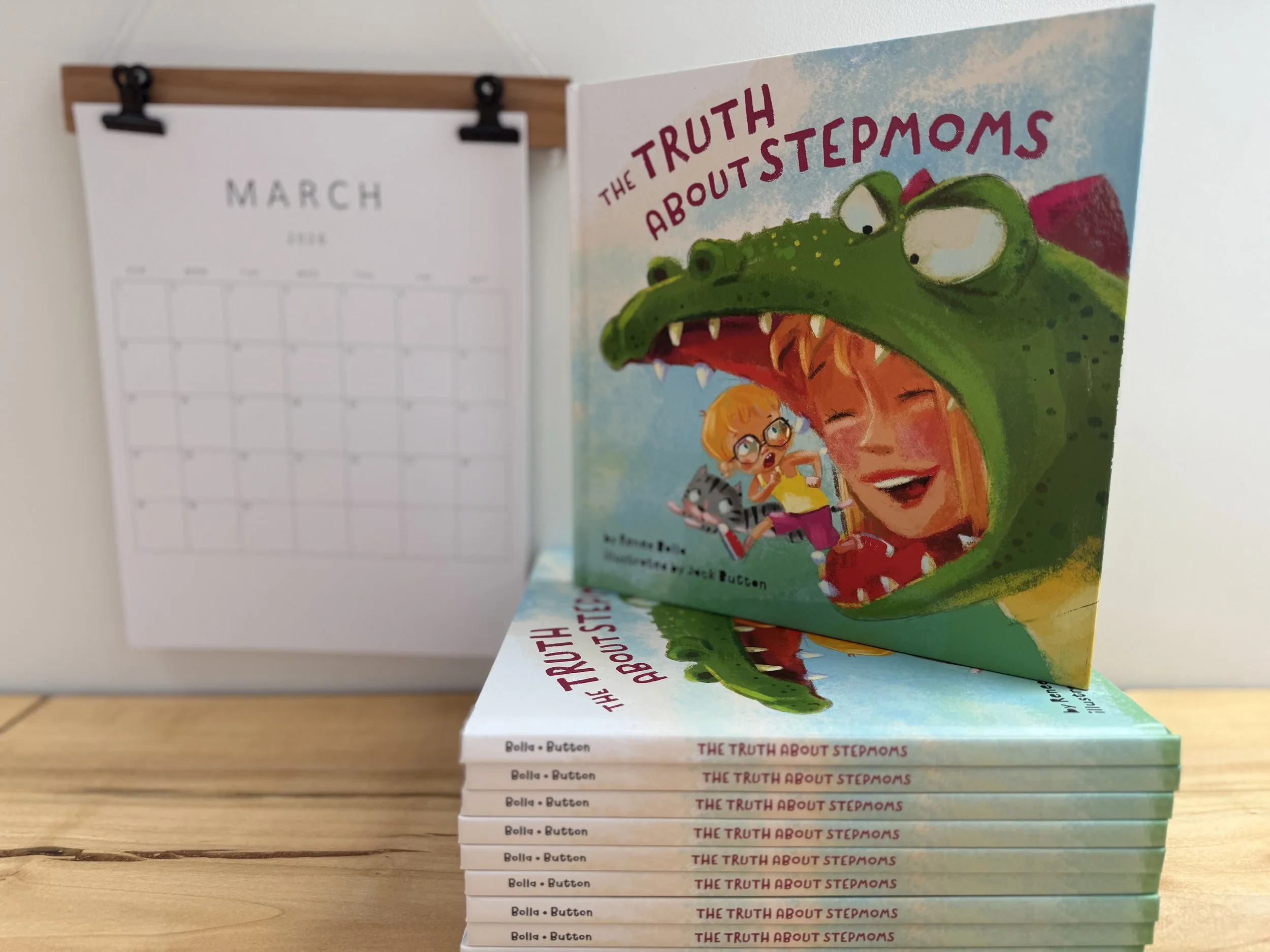 stack of picture books titled The Truth About Stepmoms written by Renee Bolla, calendar featuring March hanging next to the stack of books