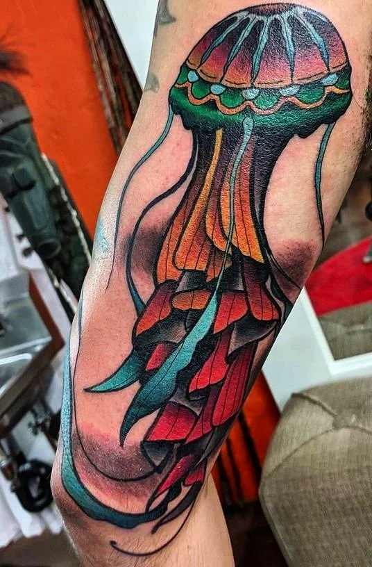 Colorful jellyfish tattoo on a person's arm featuring a large bell and trailing tentacles.