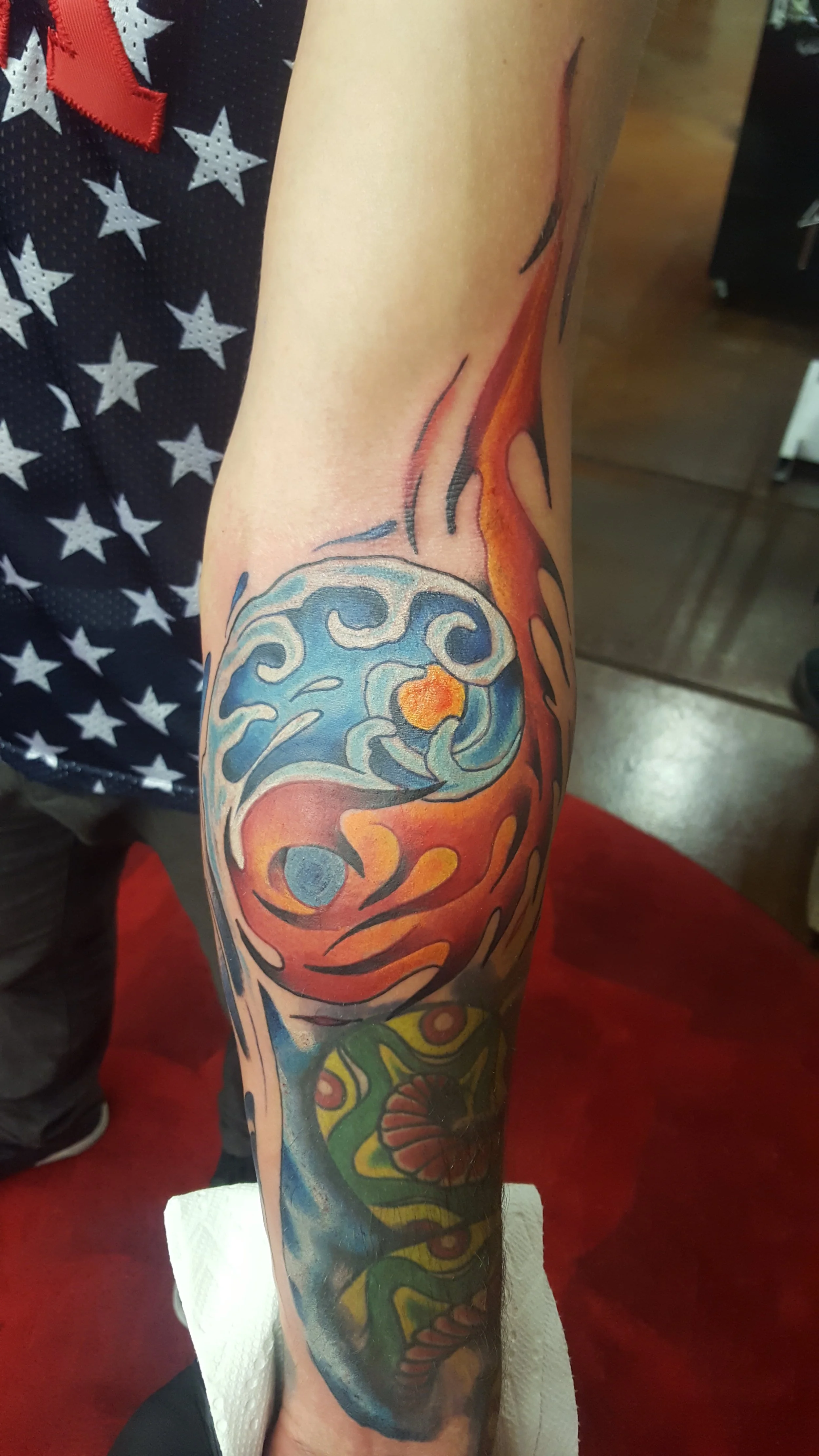 Colorful tattoo on person's arm featuring a wave and sun, with bold lines and vivid colors.