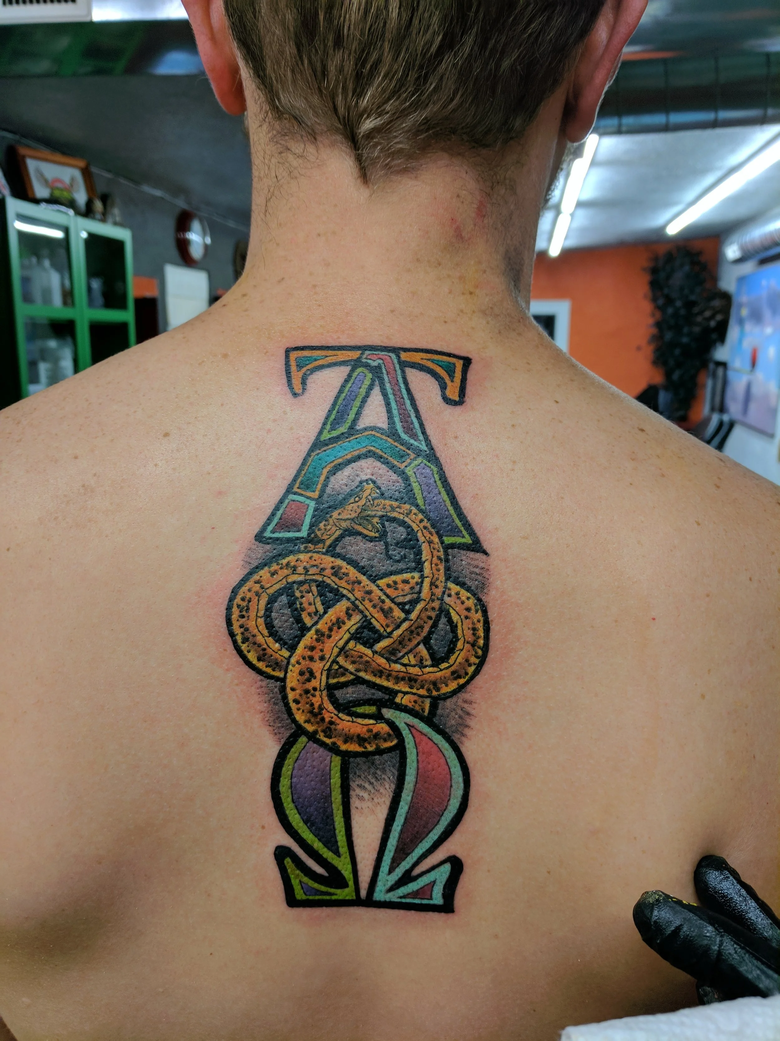 Colorful tattoo of the number 12 with a snake intertwined through it on a person's upper back.