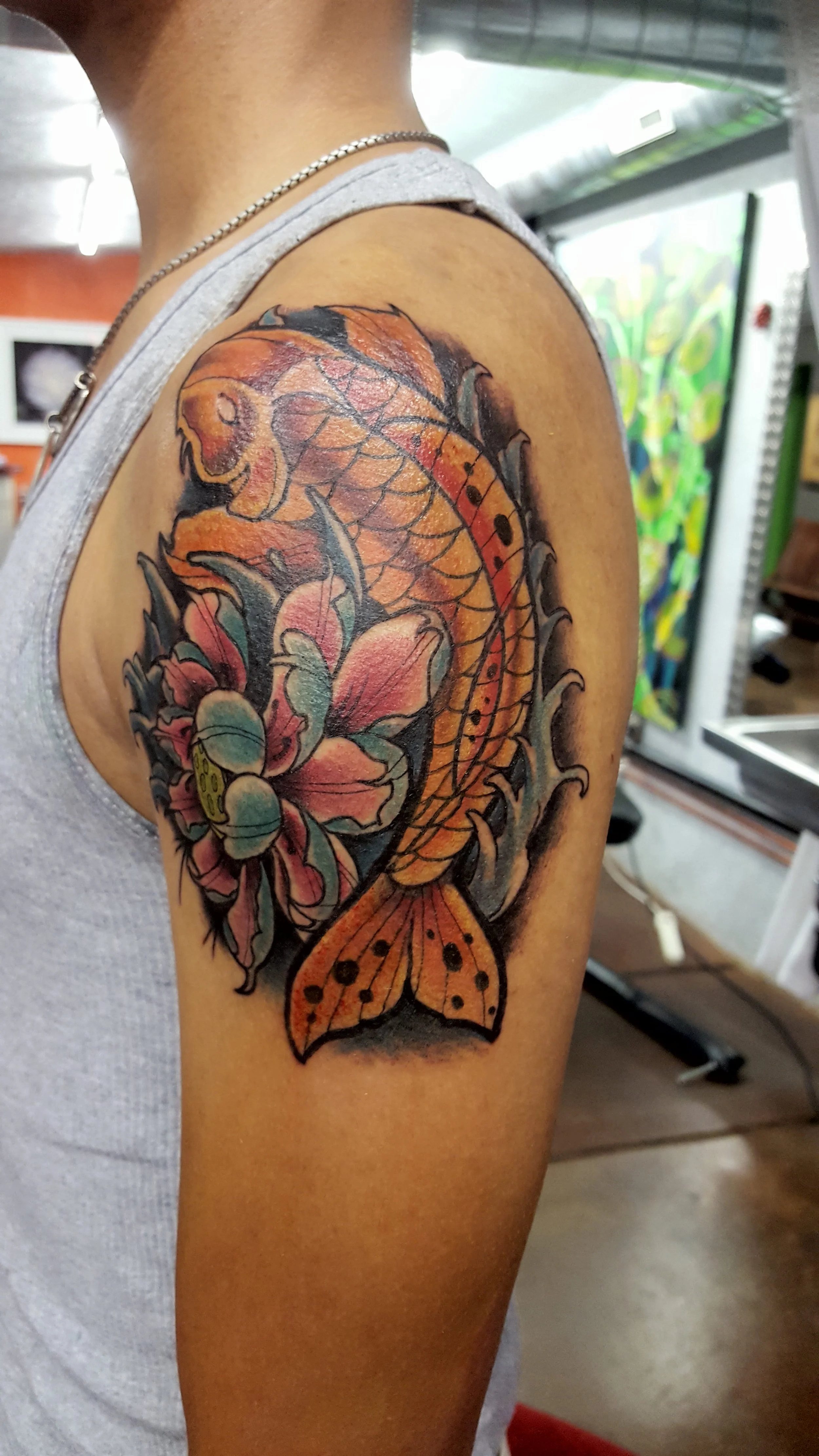Colorful tattoo of a koi fish swimming around a pink and blue flower on person's upper arm.