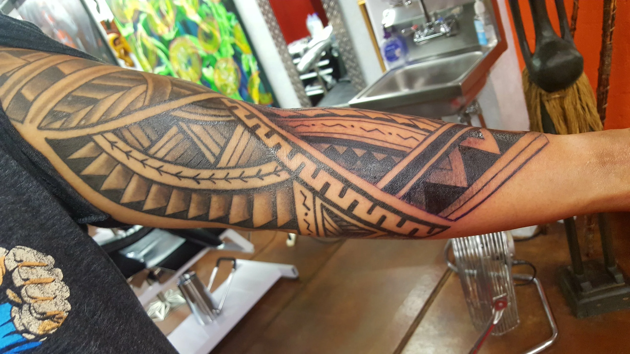 Close-up of a person's arm with traditional Polynesian-style tattoo featuring black geometric patterns and designs.