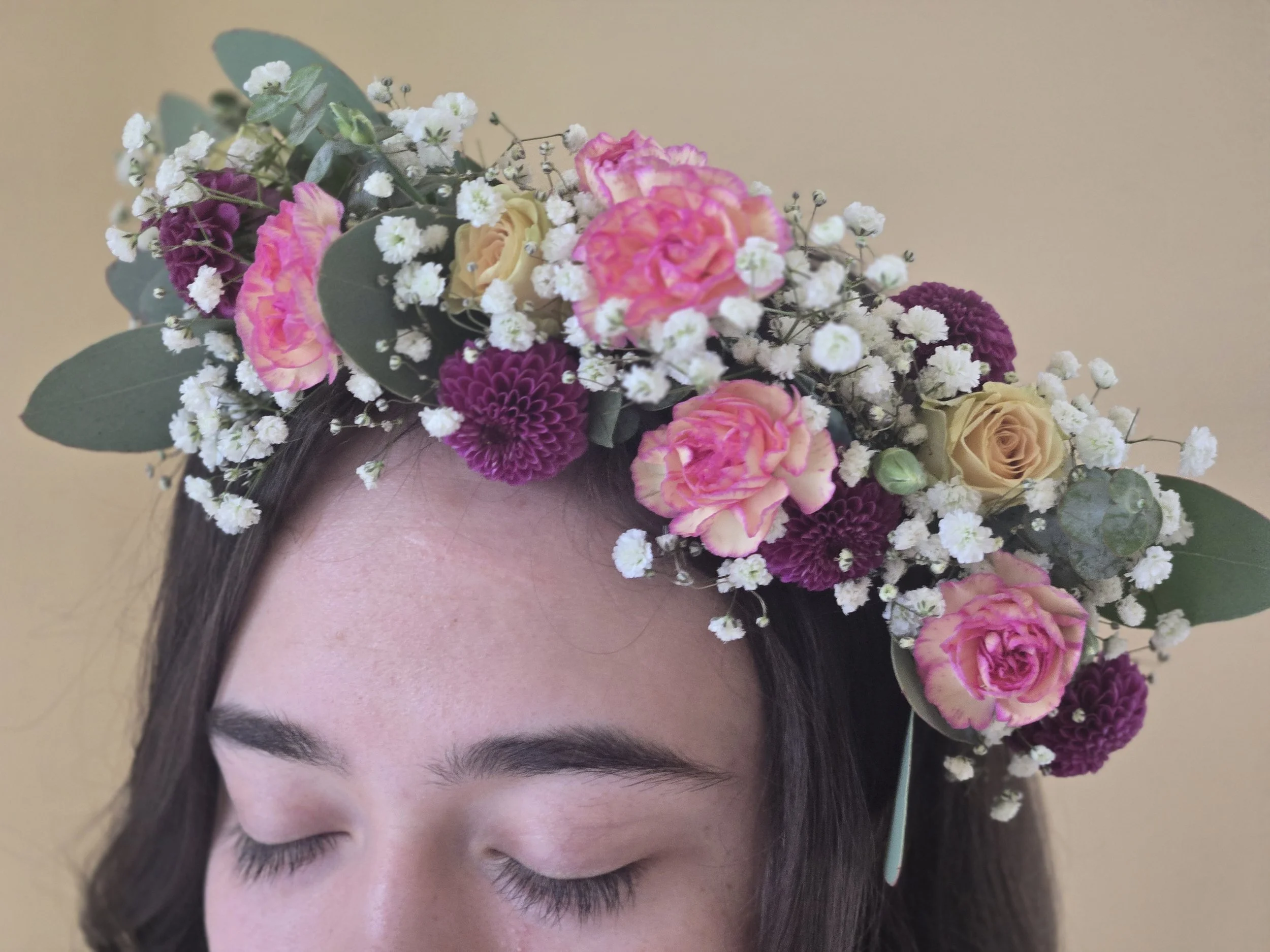 Outdoor table with floral arrangements in glass vases wrapped in plastic, set on a white tablecloth in a backyard with green grass and a wooden fence.