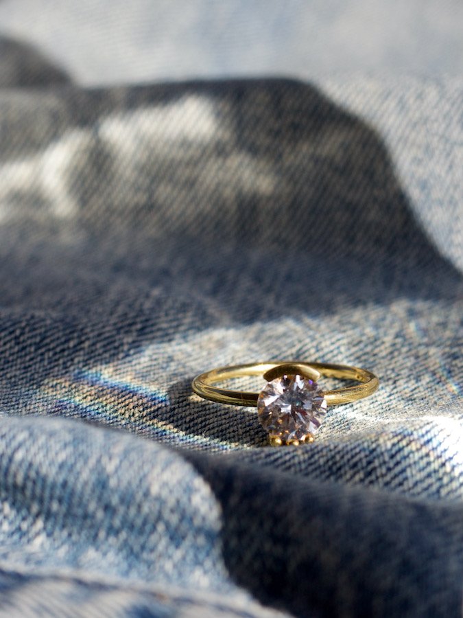 bario neal's 1.5 carat lash diamond engagement ring close up on denim with gold lash detailing for setting