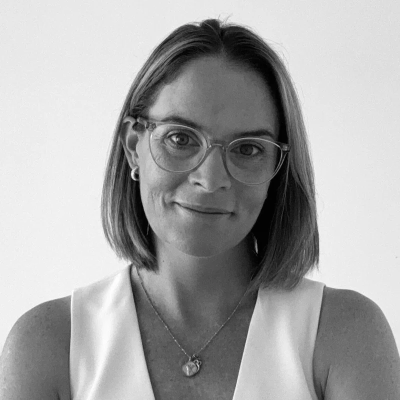 Black and white portrait of a woman with shoulder-length hair, wearing glasses, earrings, a necklace with a heart-shaped pendant, and a sleeveless top.