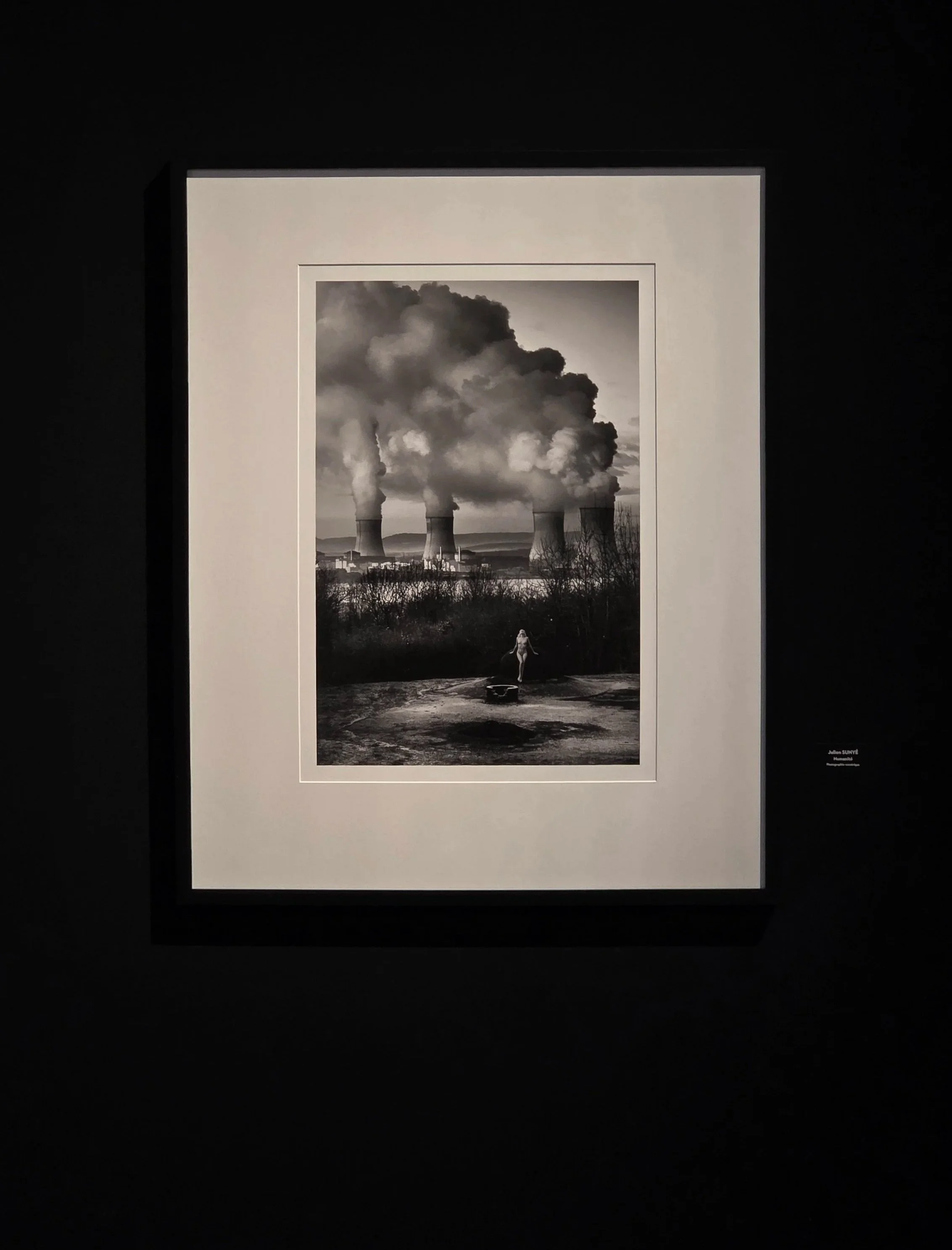 Black and white photograph of four large cooling towers emitting thick steam, with a person walking on top of the Galgenberg bunker from France's Maginot defense line.