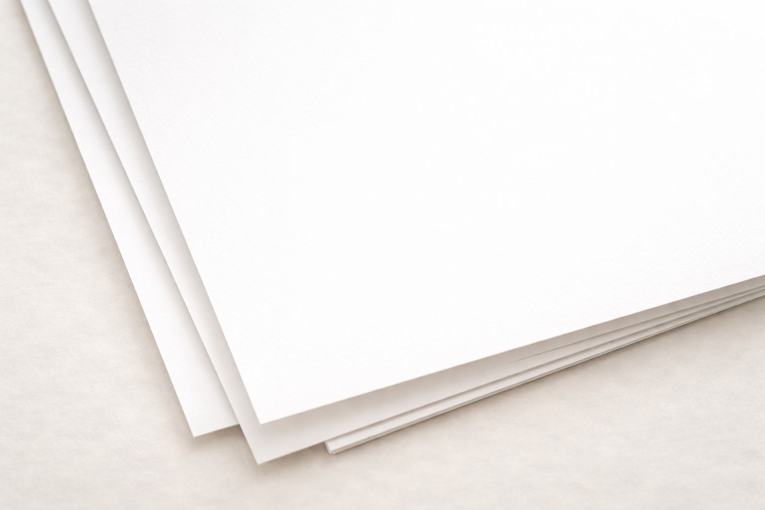 Stack of blank white sheets of paper on a light-colored surface.