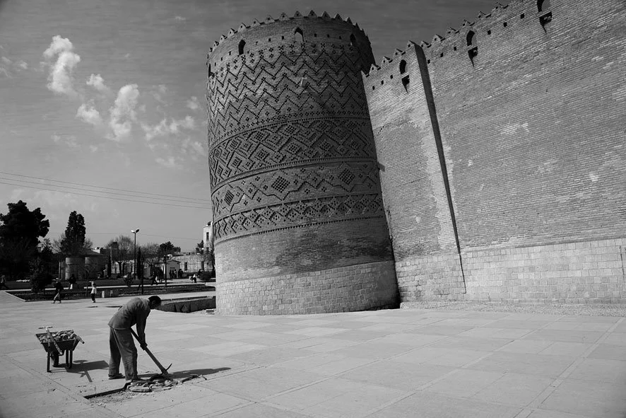 A man working on a sidewalk near an ancient brick fortress wall with decorative patterns.
